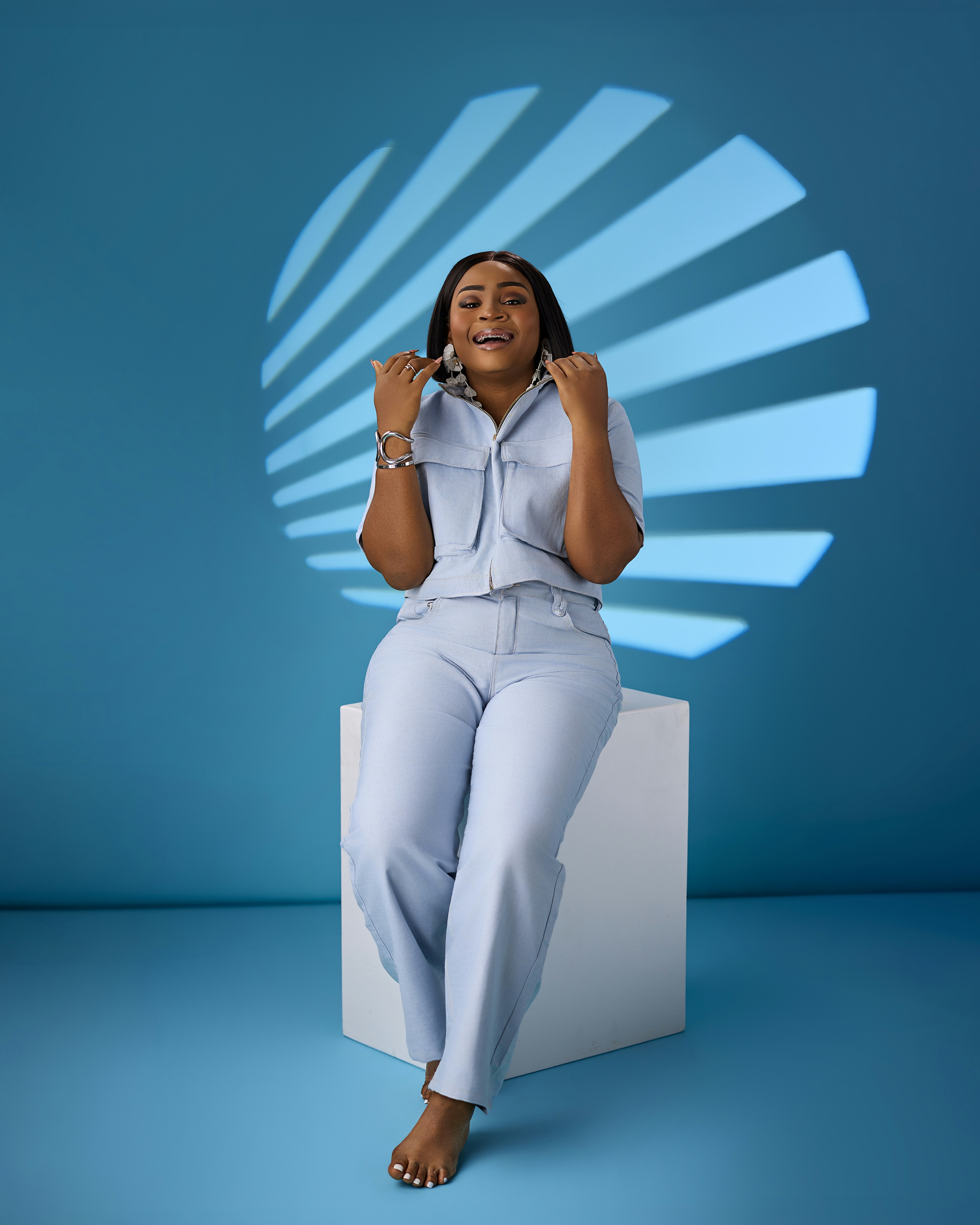 A woman in a light blue denim outfit sitting on a white cube