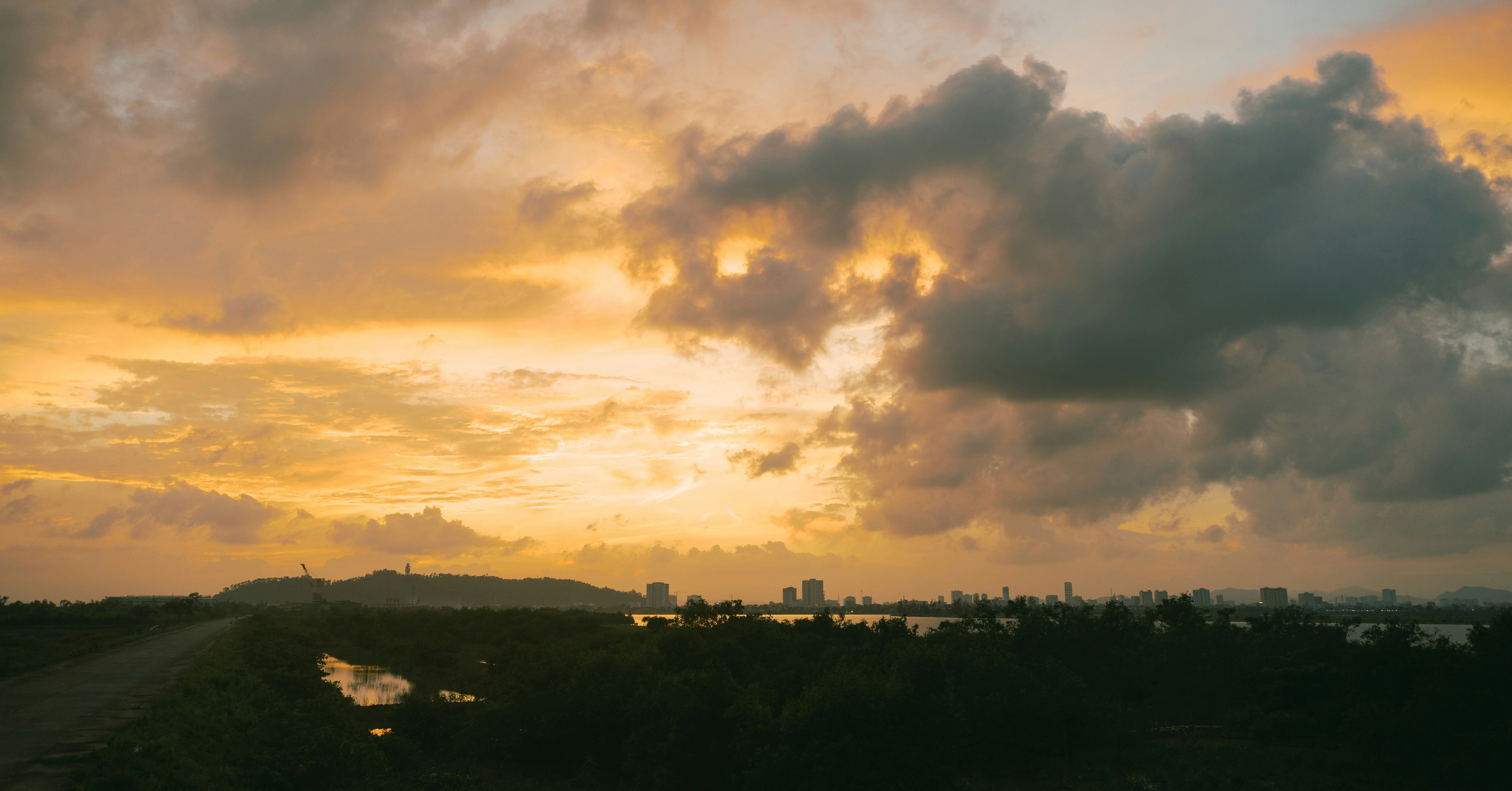 A distant city skyline silhouetted against a warm orange sky with dark clouds