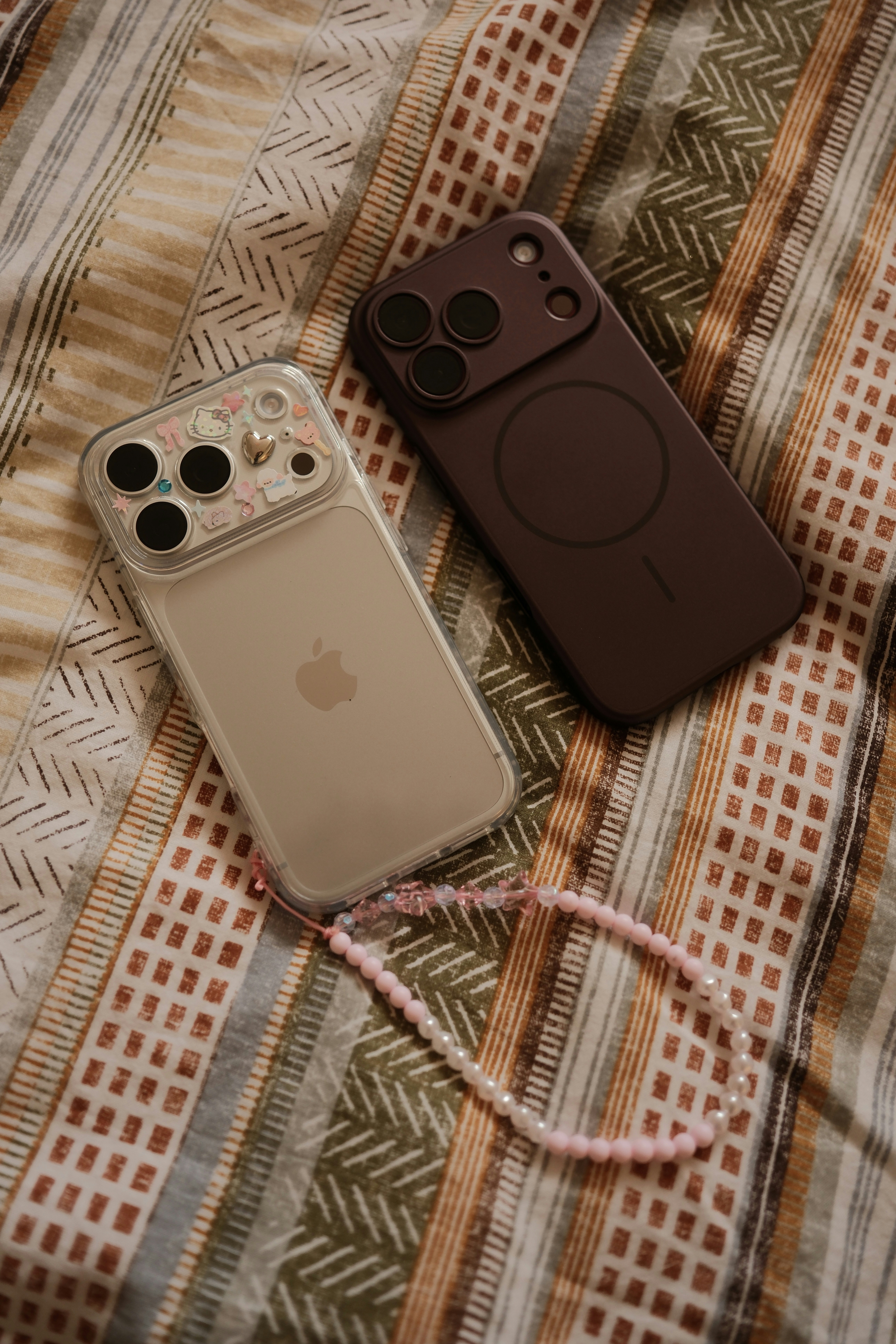 Two smartphones on a patterned fabric surface with a beaded phone charm