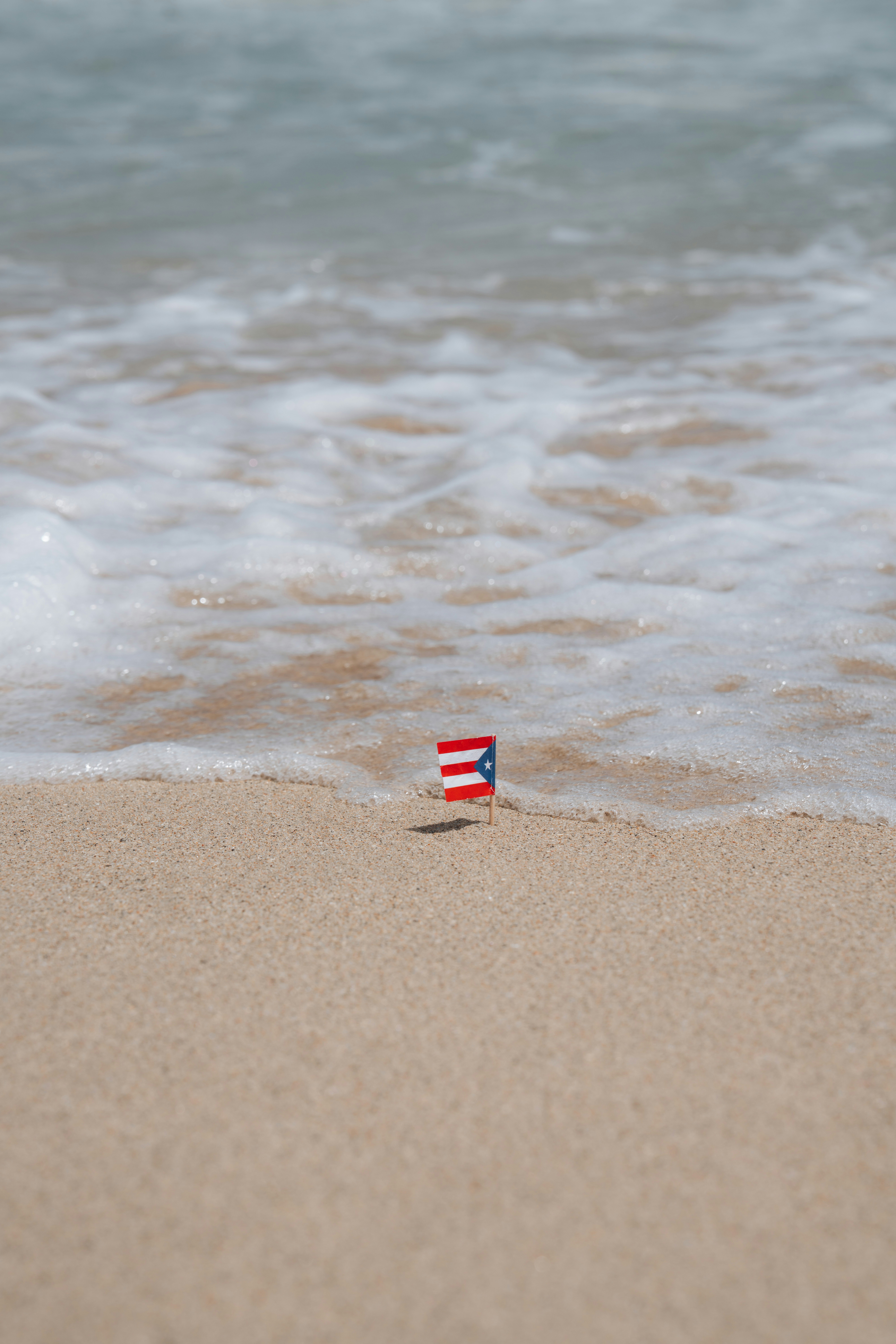 A small Puerto Rican flag stuck in the sand at the water's edge