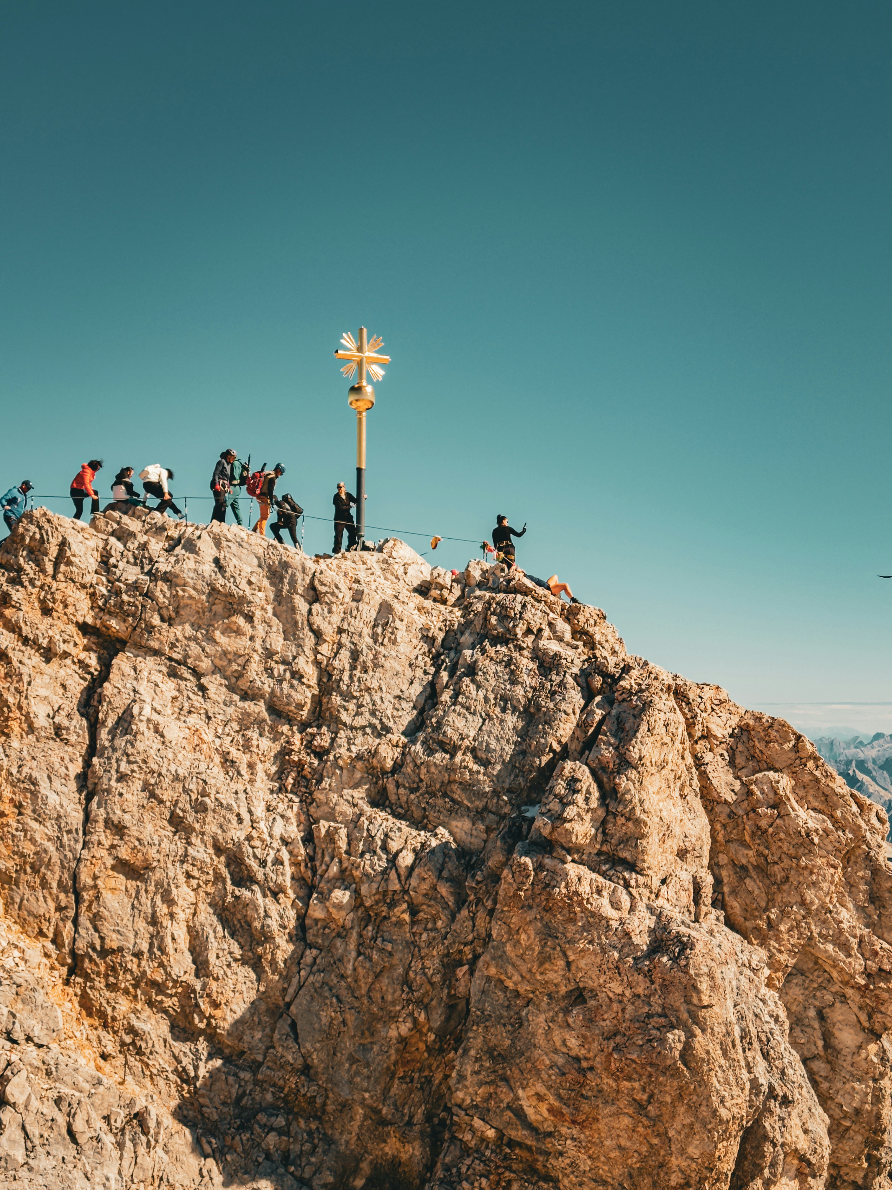 A group of people on a rocky mountain summit with a golden cross