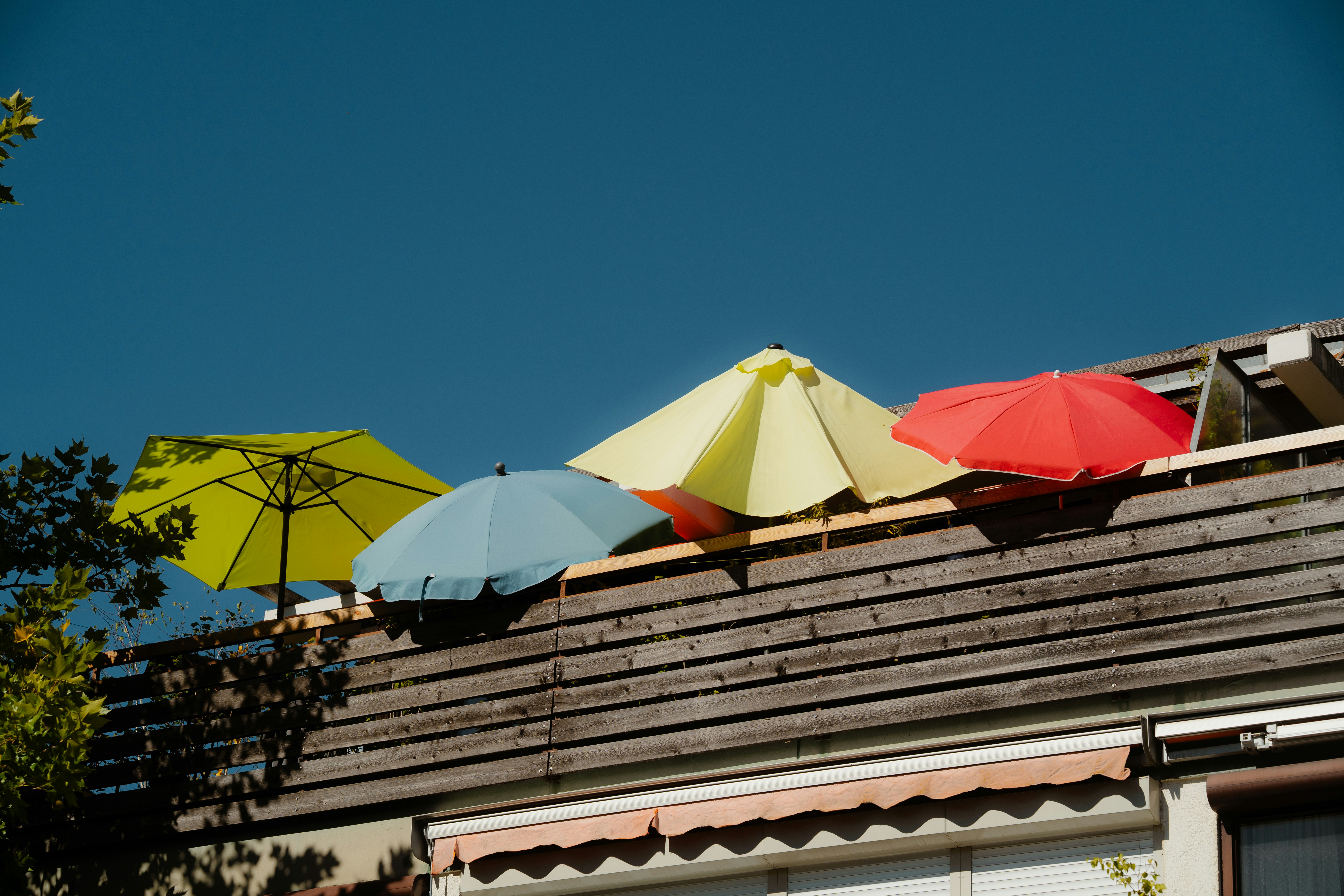 Four colorful patio umbrellas on a wooden balcony against a clear blue sky