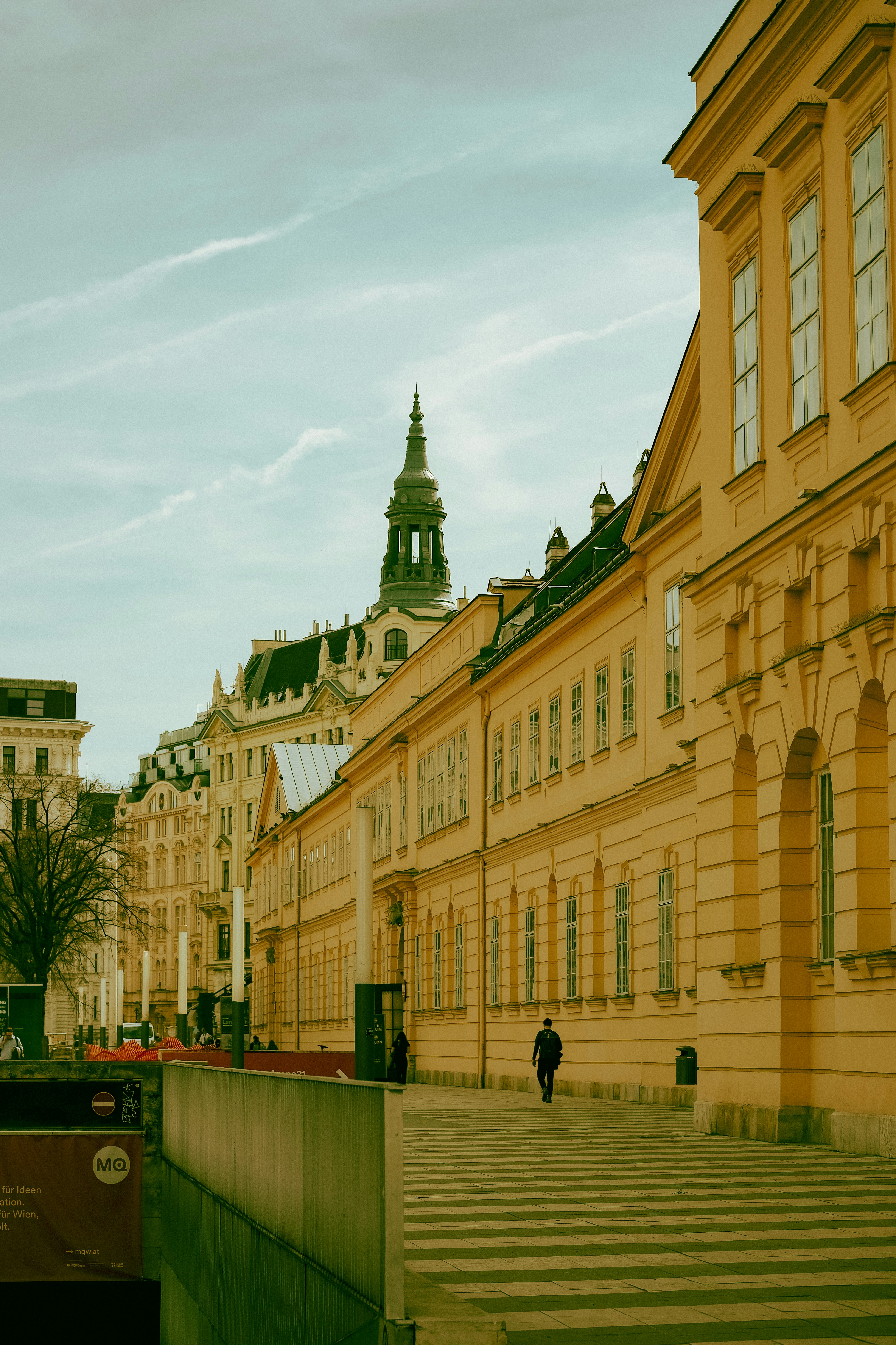 A person walking along a striped sidewalk beside a yellow historic building in Vienna