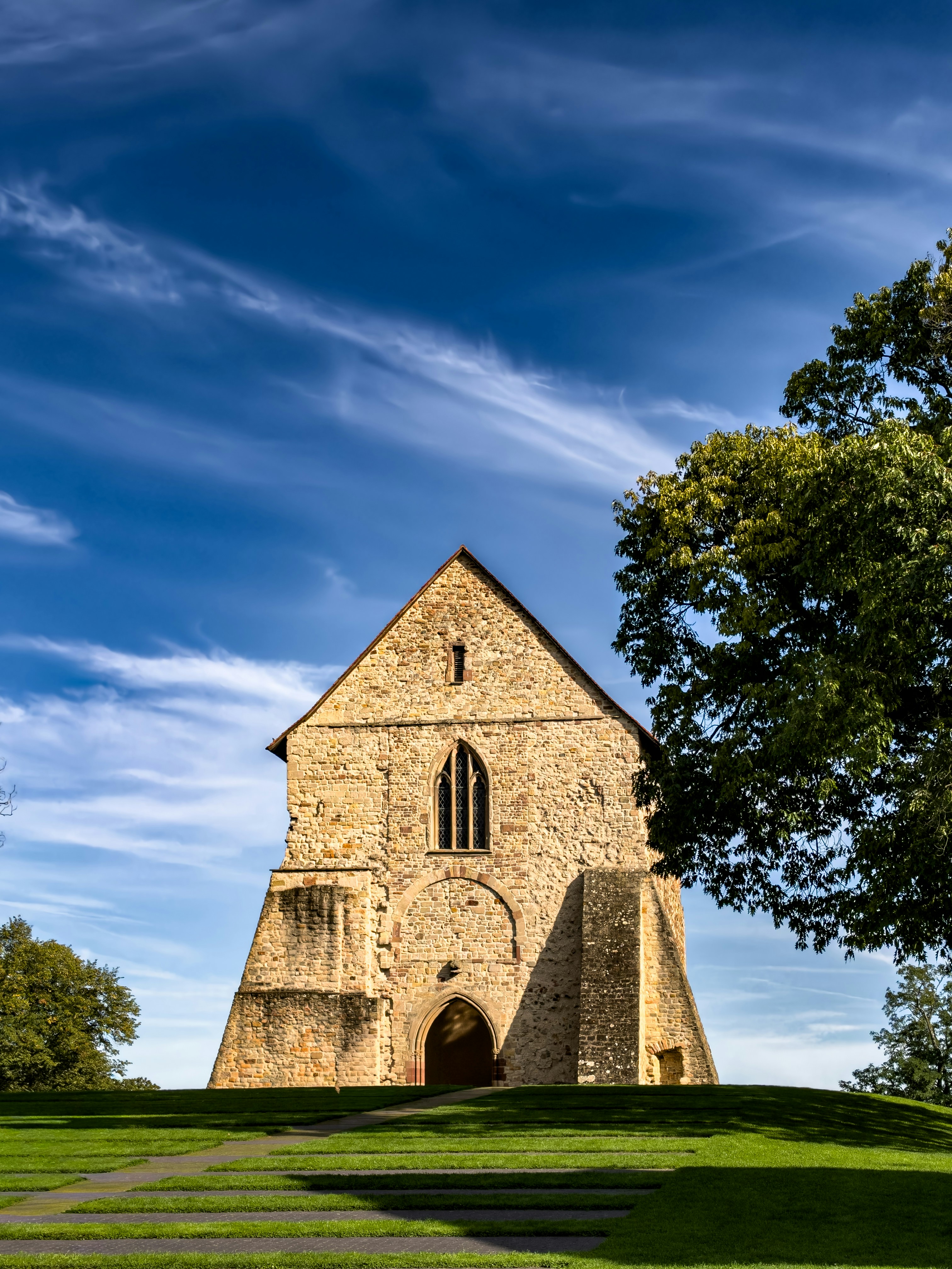 A stone church building on a grassy hill under a blue sky with clouds