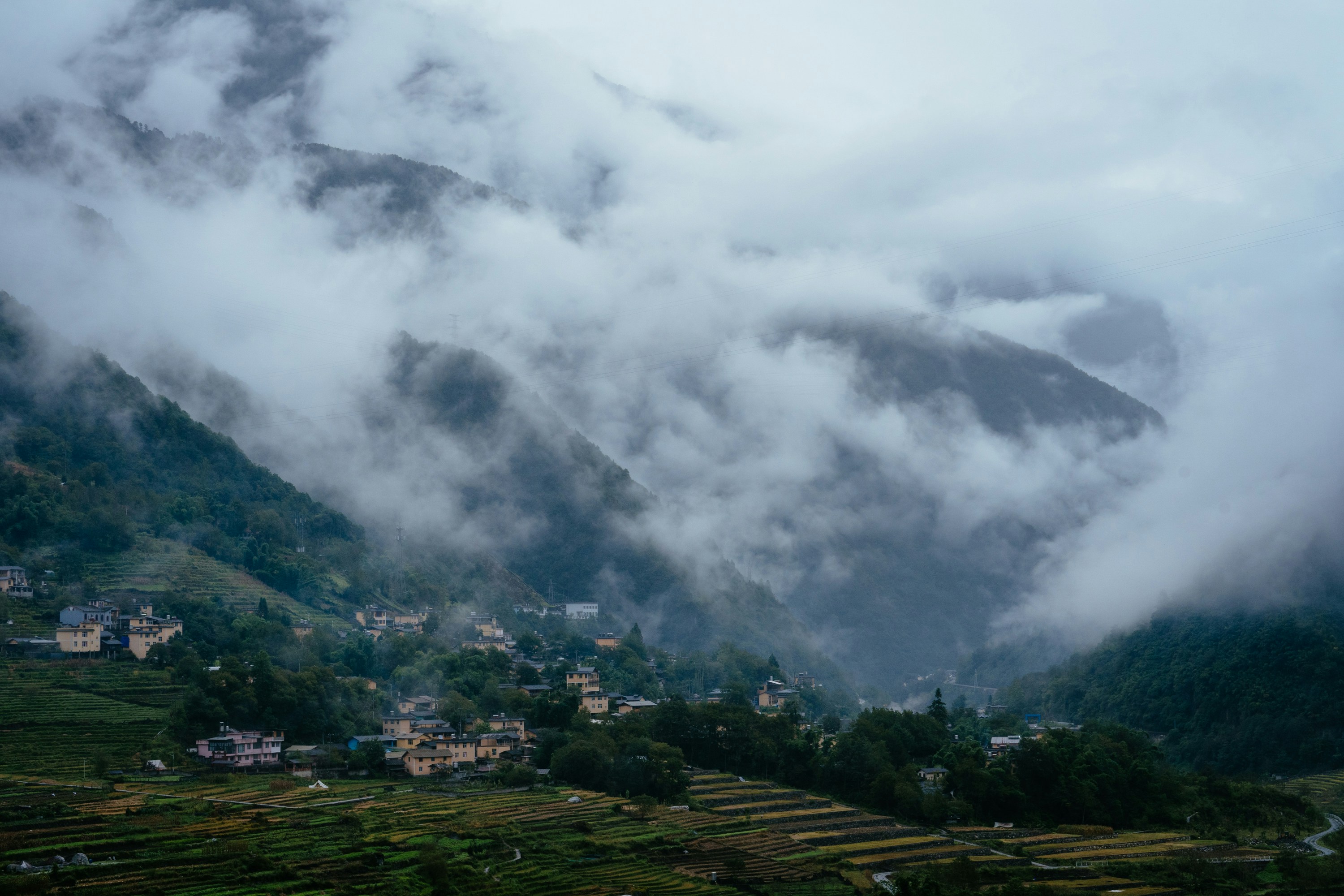 A village nestled among terraced fields and mountains shrouded in thick low clouds