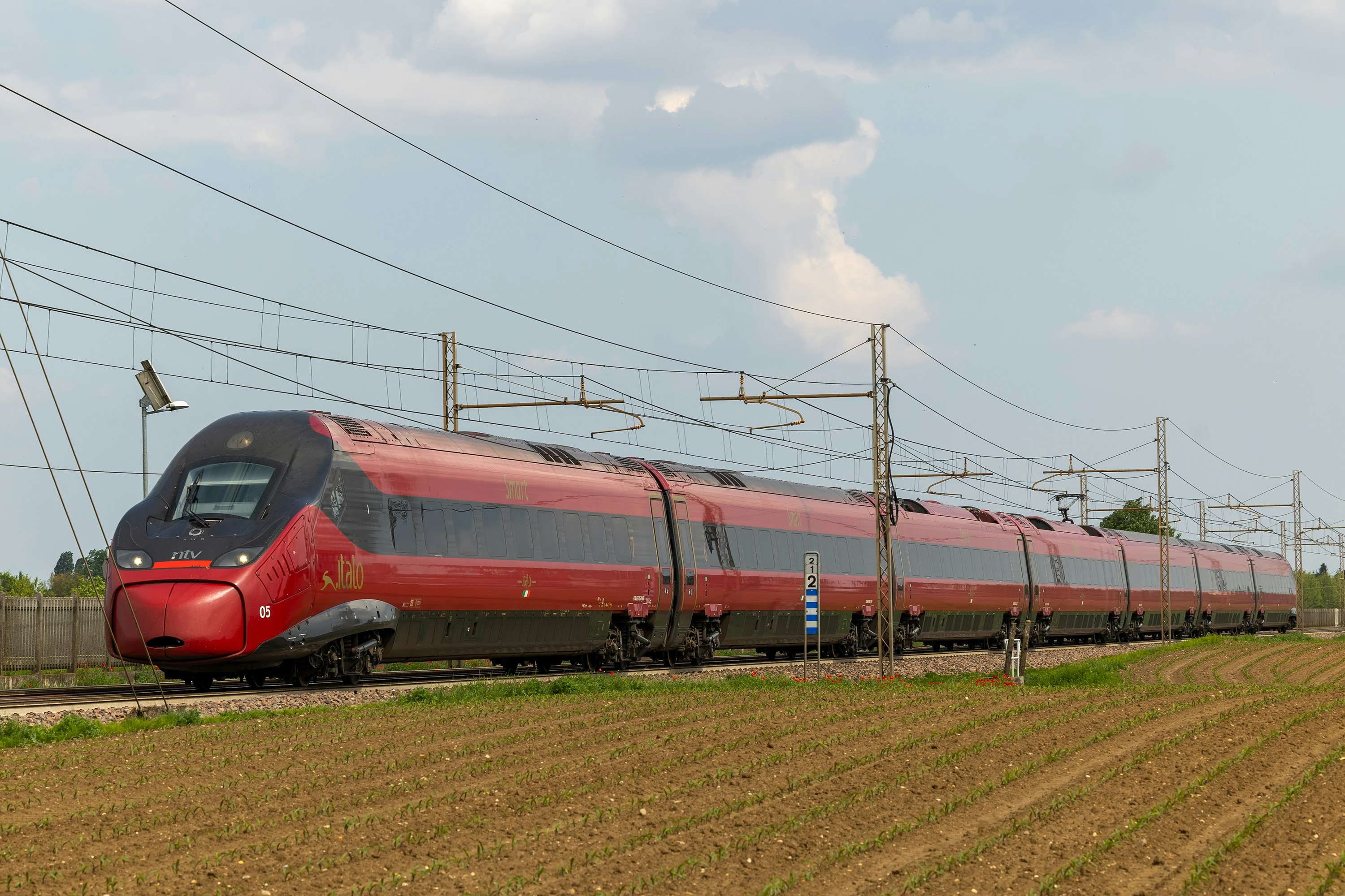 Un train Italo rouge à grande vitesse circulant sur des rails à travers un paysage rural