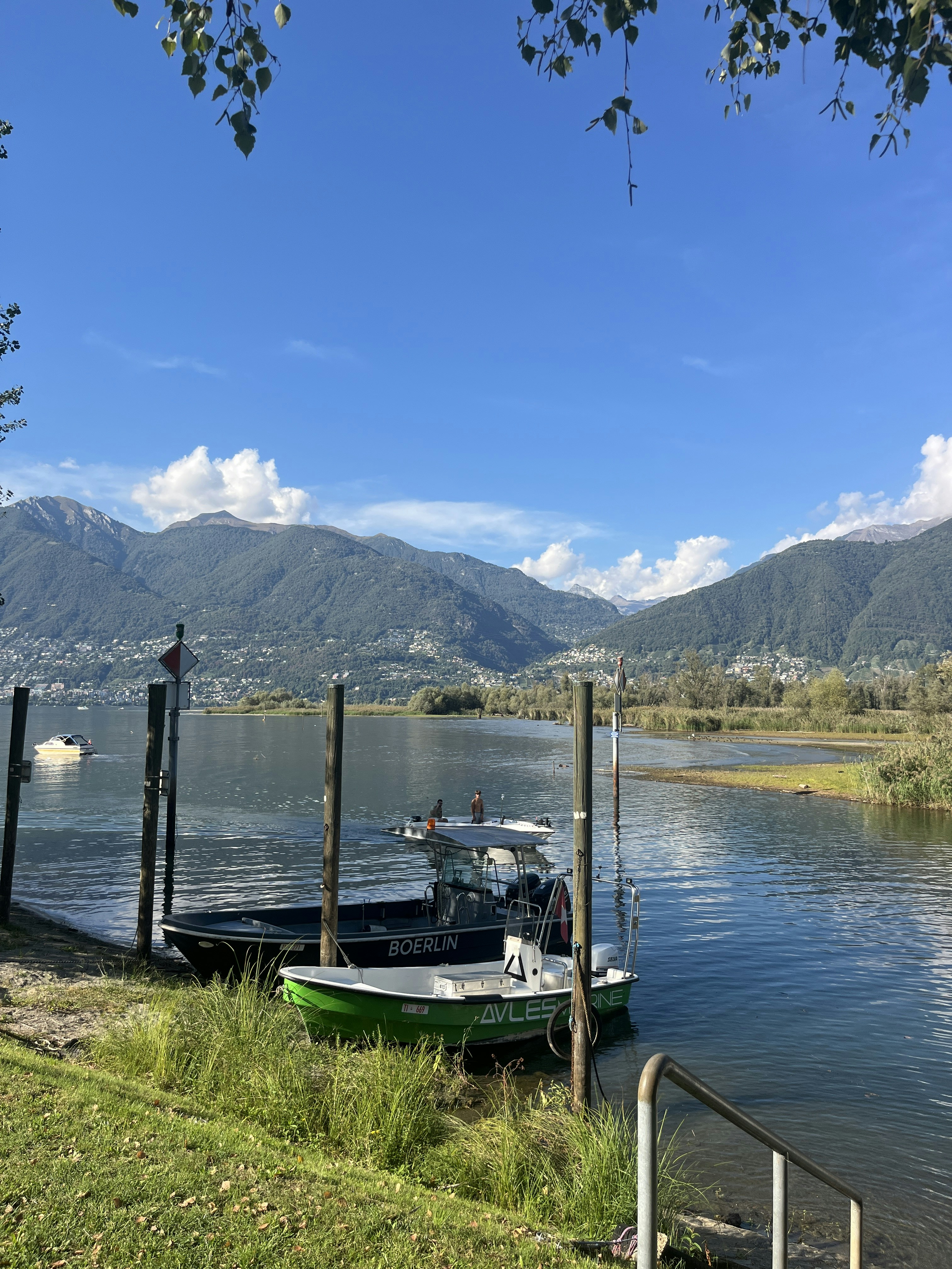 Two motorboats moored at a wooden pier on a lake with mountains behind