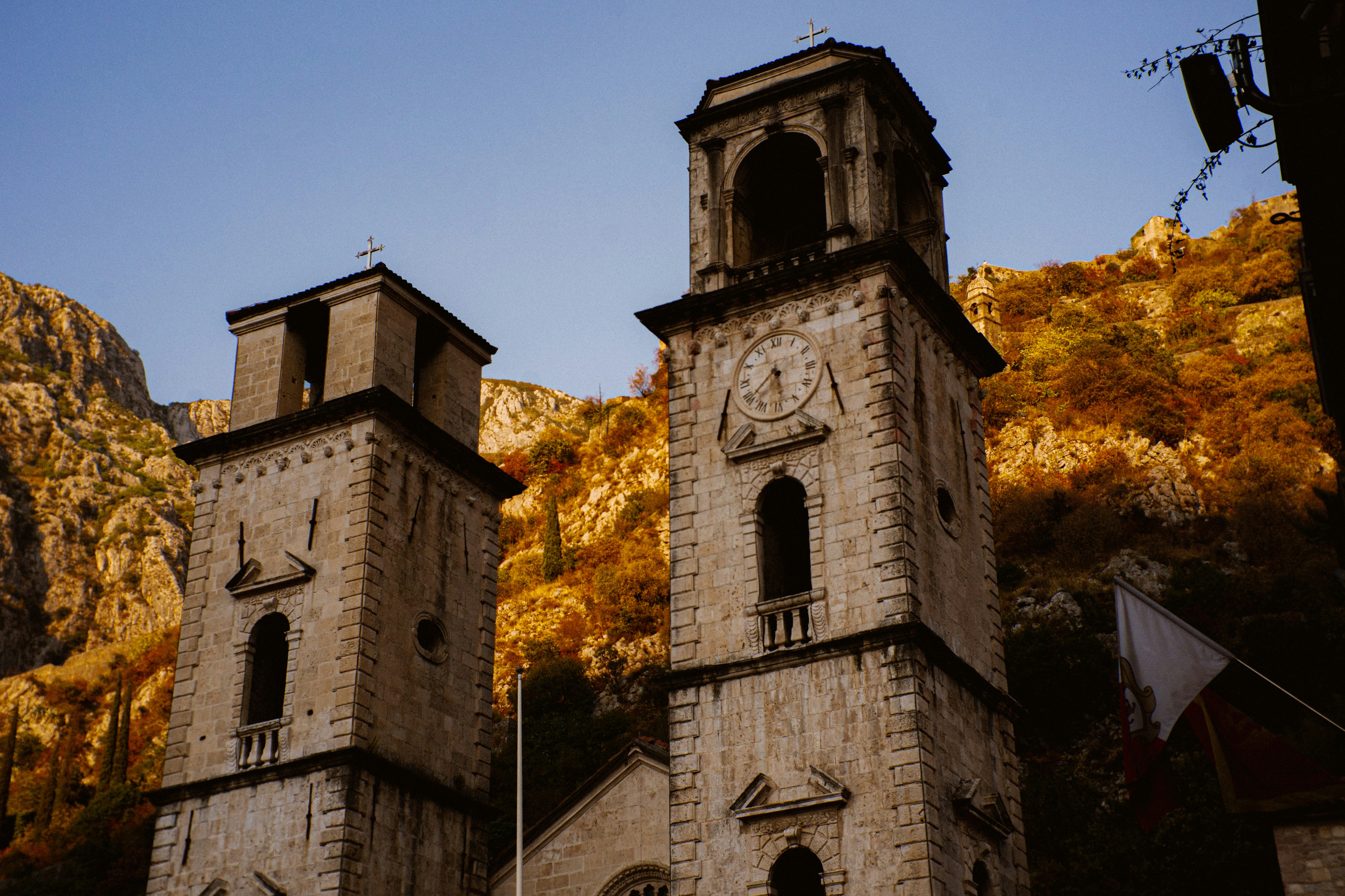 Two stone bell towers with crosses against a rocky mountain at golden hour