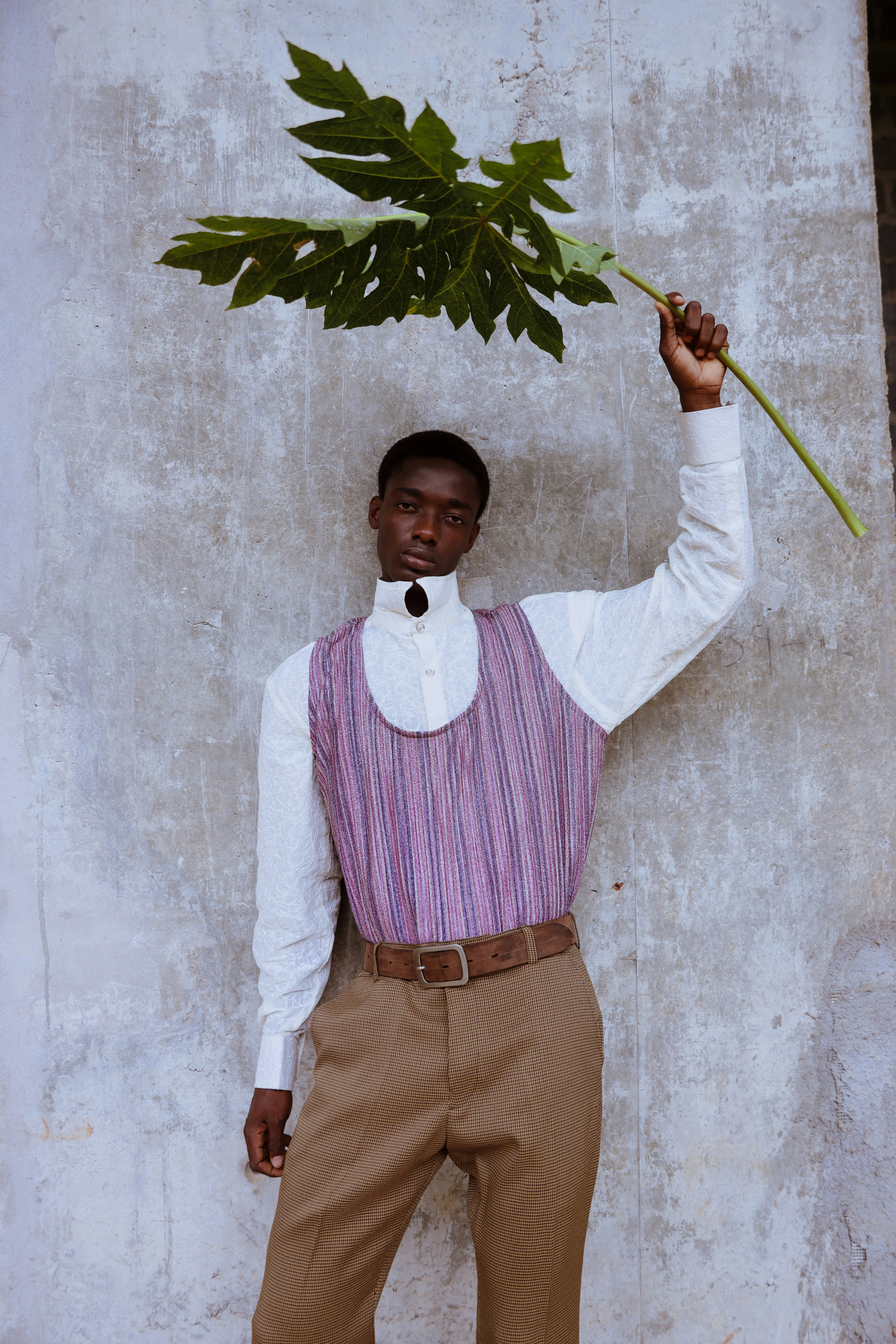 A man in a white shirt and purple vest holding a large green leaf