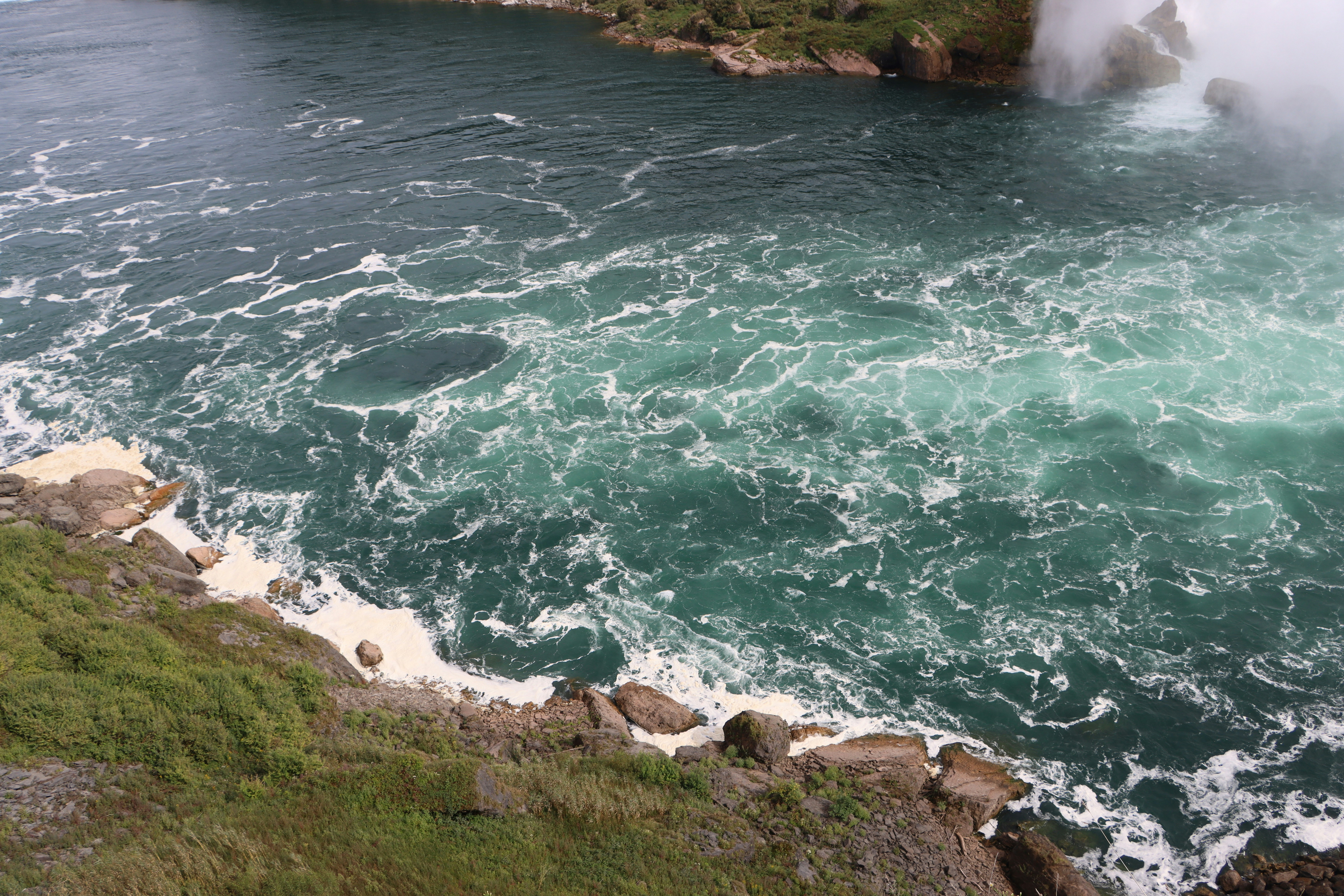 Churning turquoise water with white foam along a rocky shoreline at Niagara Falls