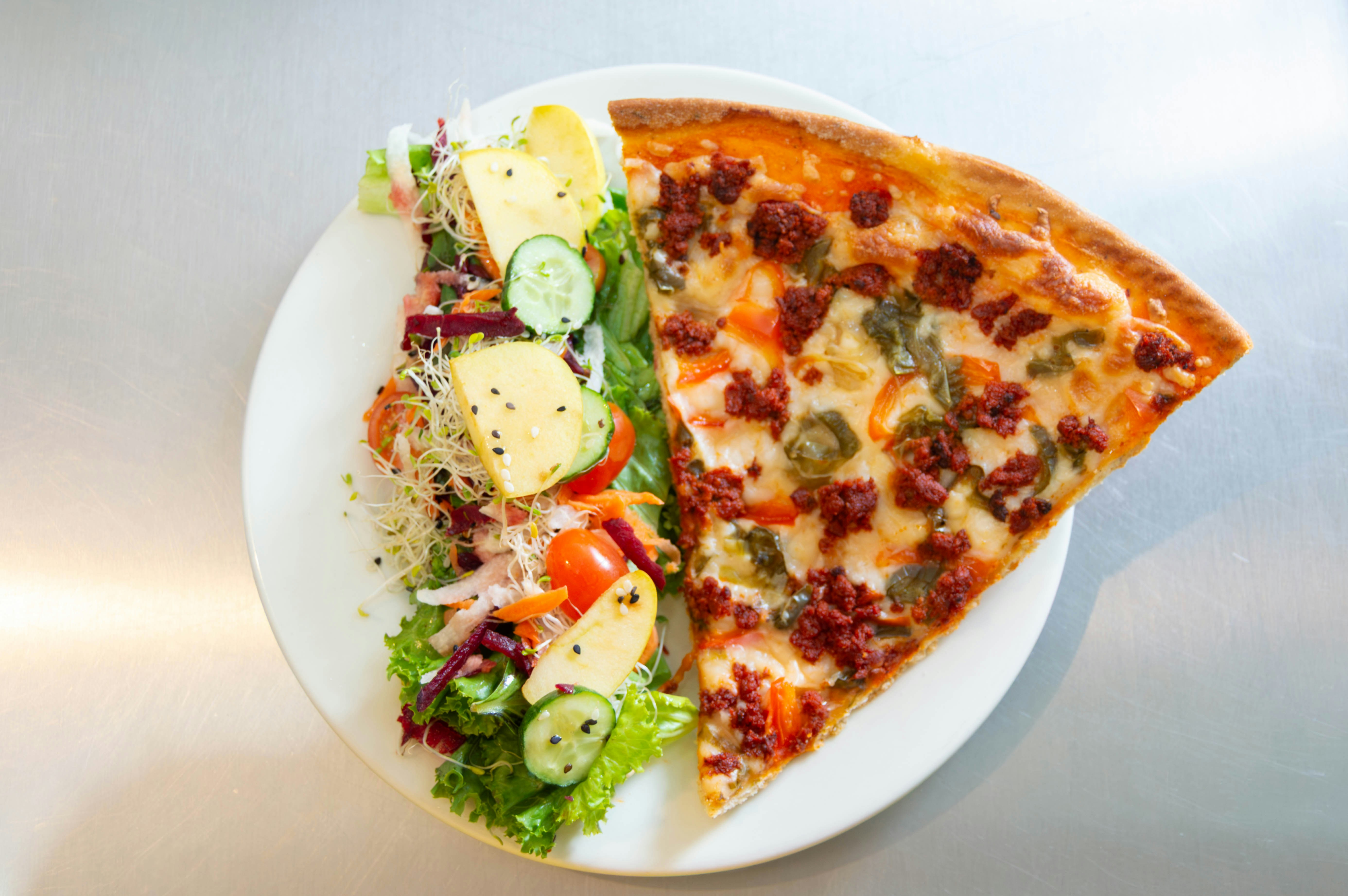Slice of chorizo pizza beside a fresh salad
