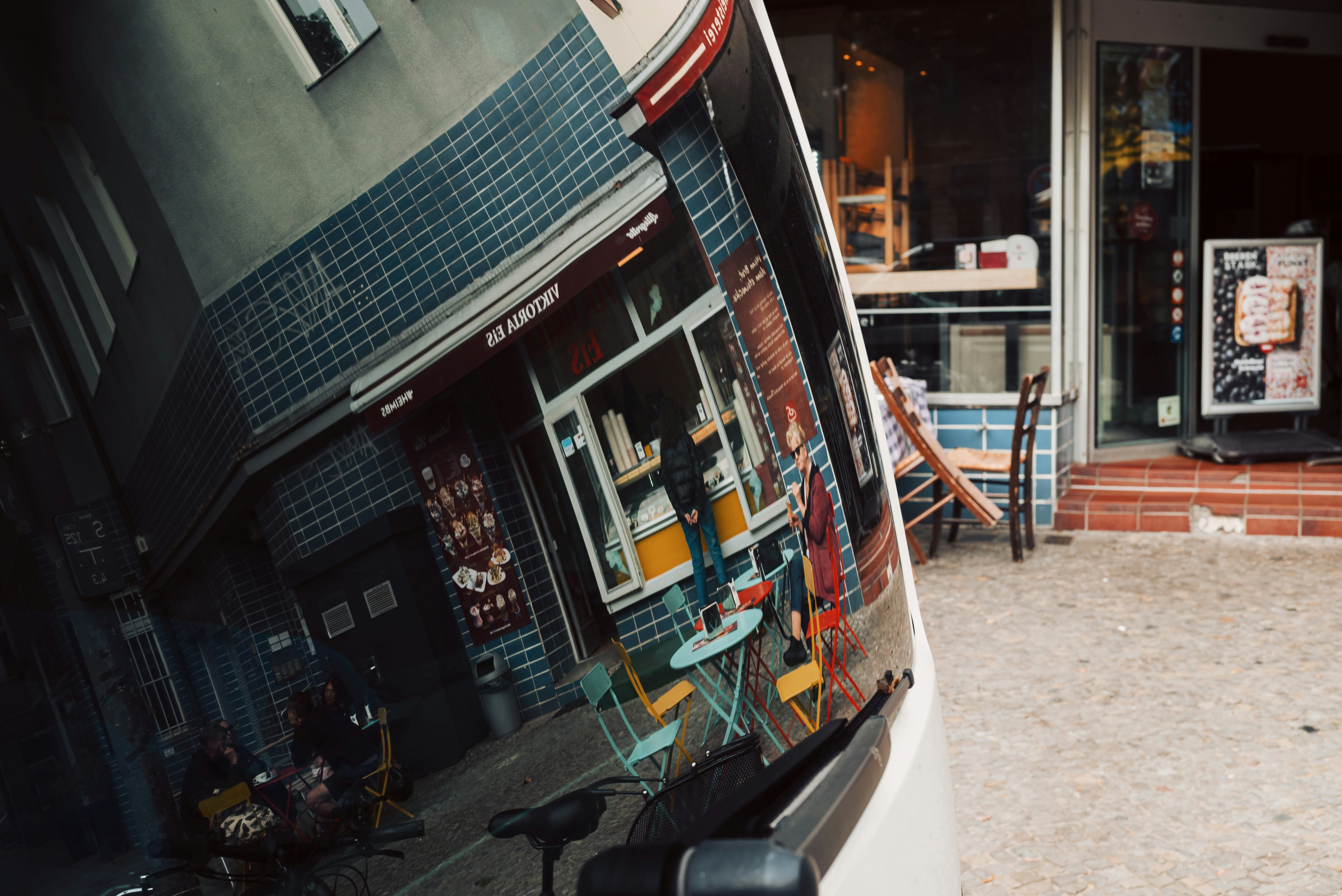 Refleksi kafe dengan tempat duduk luar ruangan di cermin melengkung di Berlin