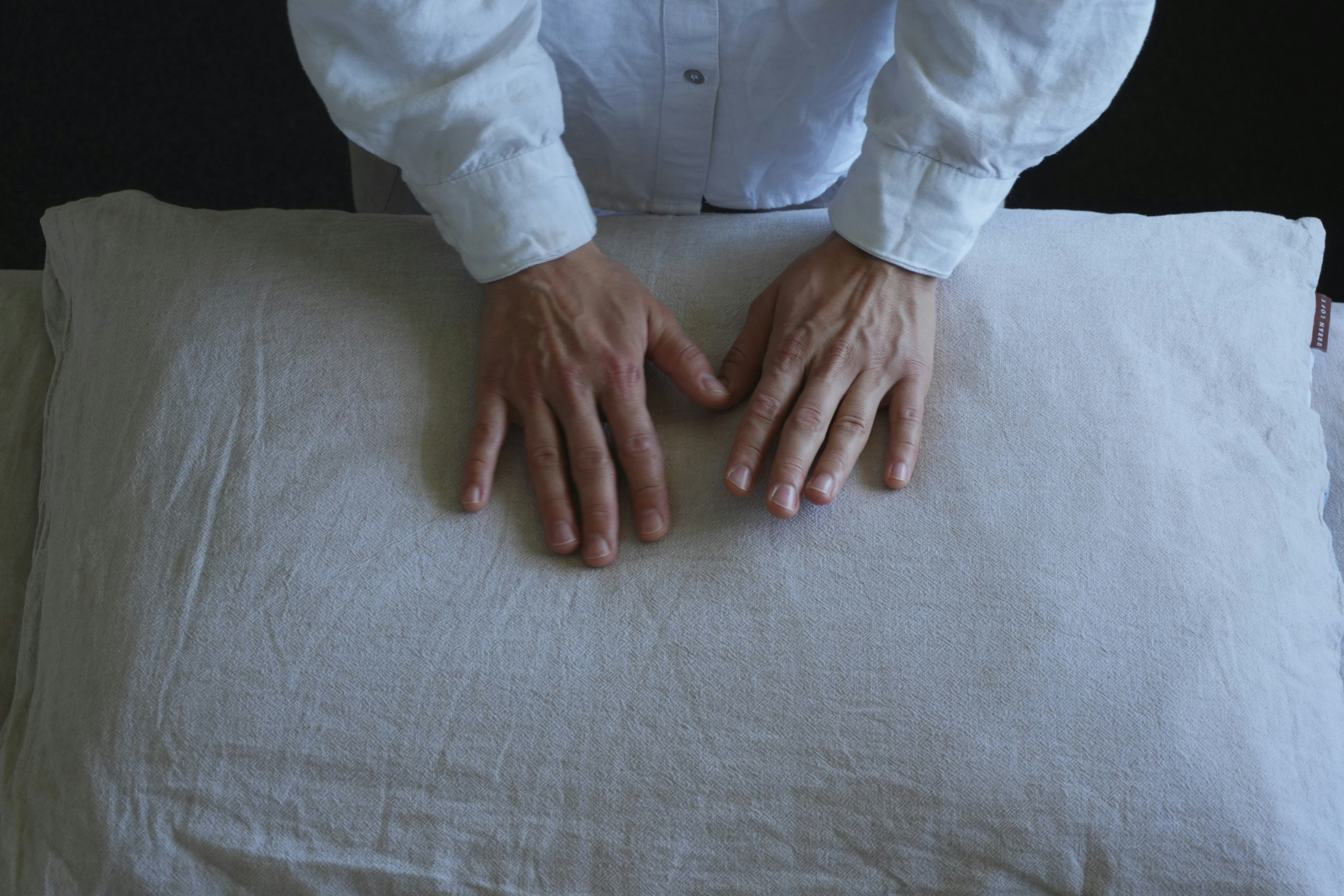 Fotomural A person in a white shirt pressing hands onto a textured linen pillow