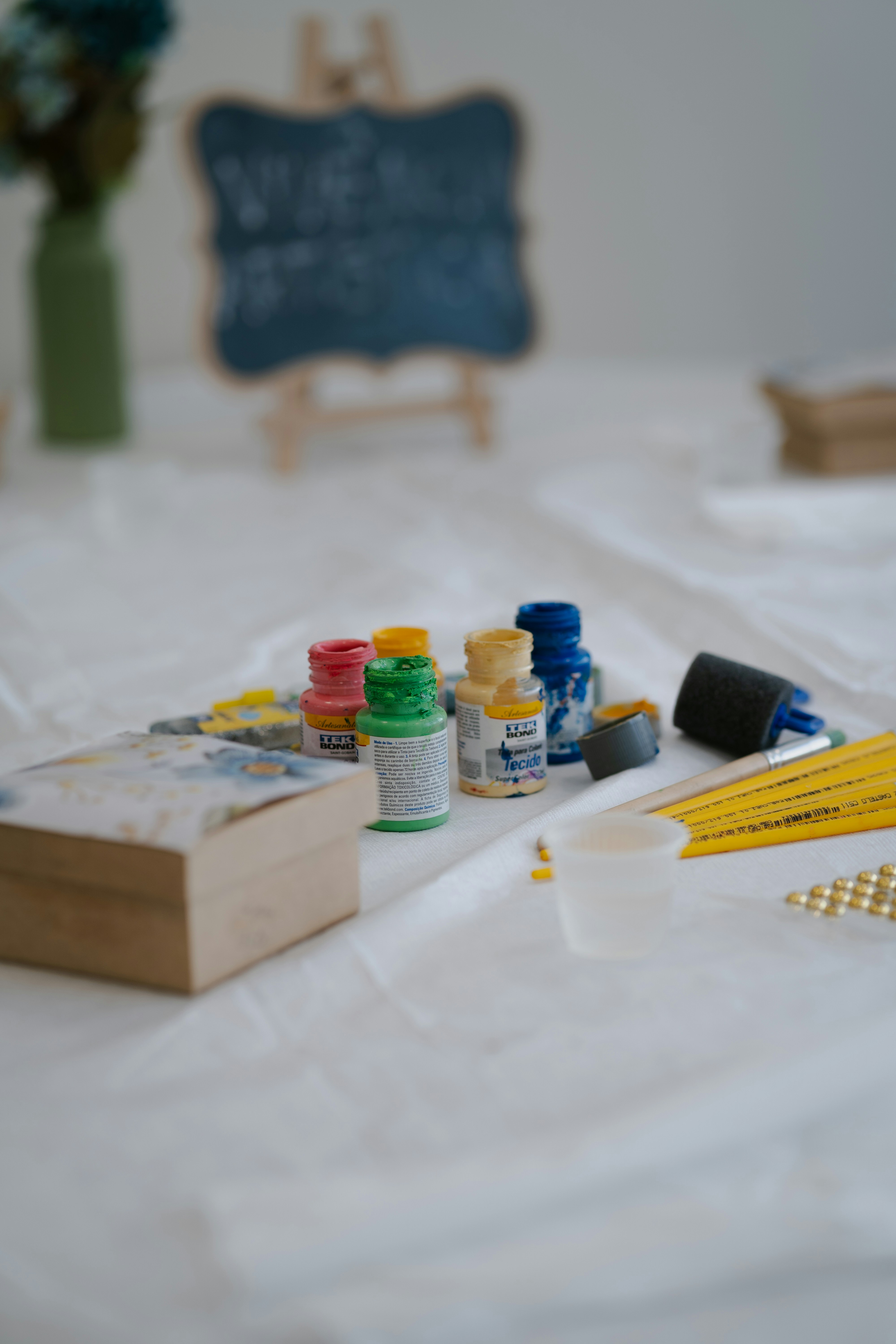 Kleine Fläschchen bunter Bastelfarbe, Pinsel und eine Holzschachtel auf weißem Stoff