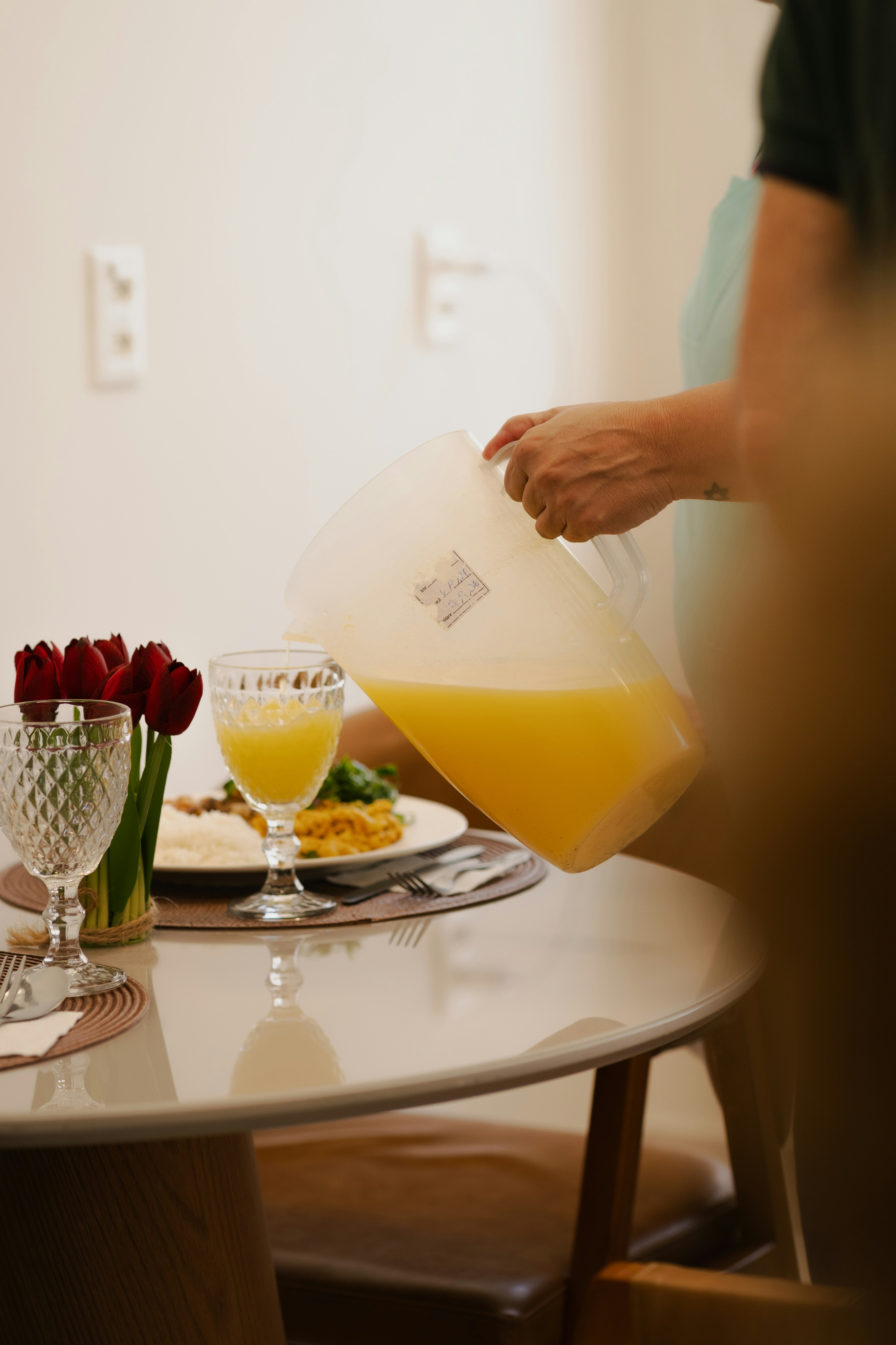 Eine Person, die Orangensaft aus einer Plastikkanne in ein Glas an einem Tisch gießt