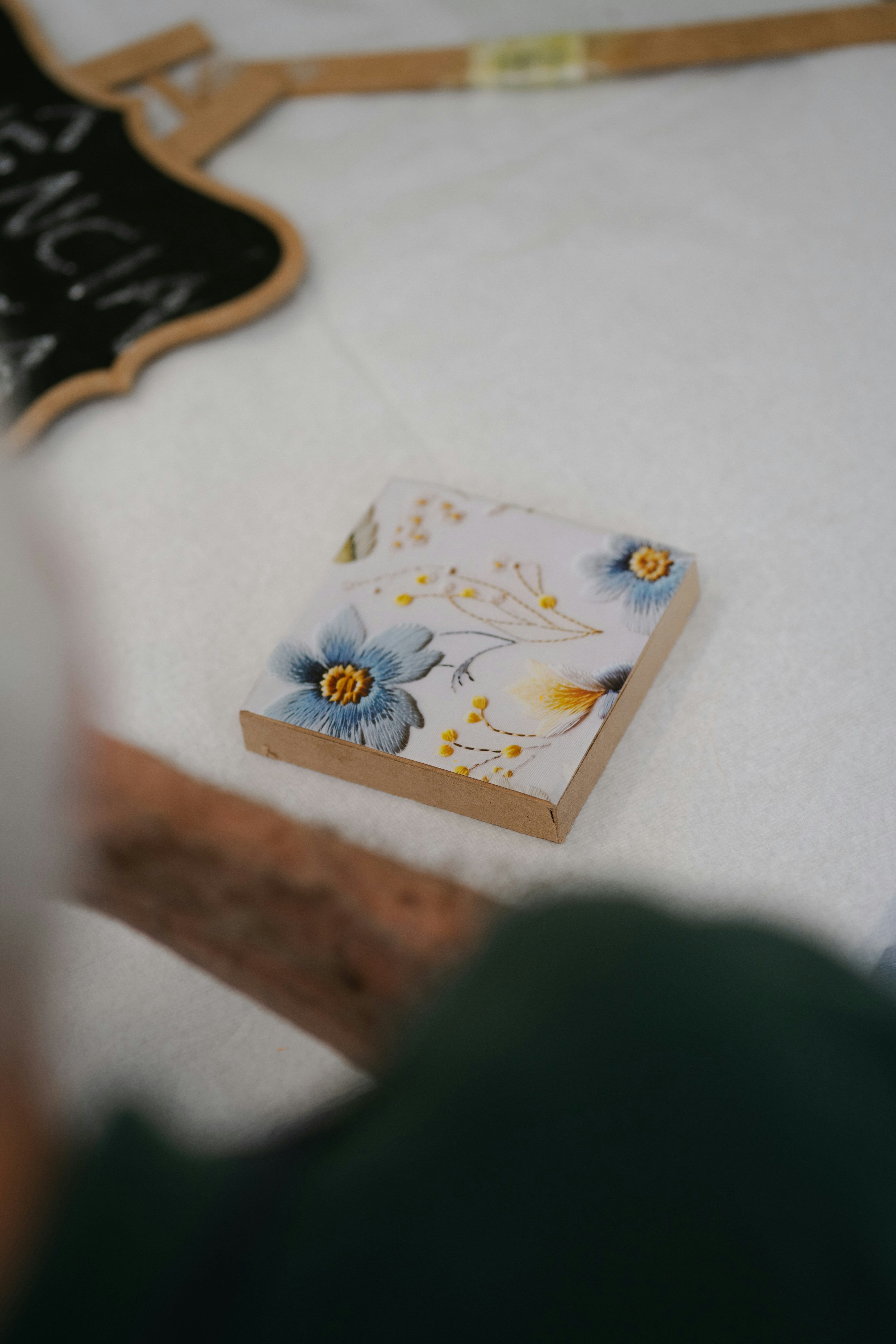 Ein kleiner quadratischer Holzblock mit bestickten blauen Blumen auf einer weißen Stoffoberfläche
