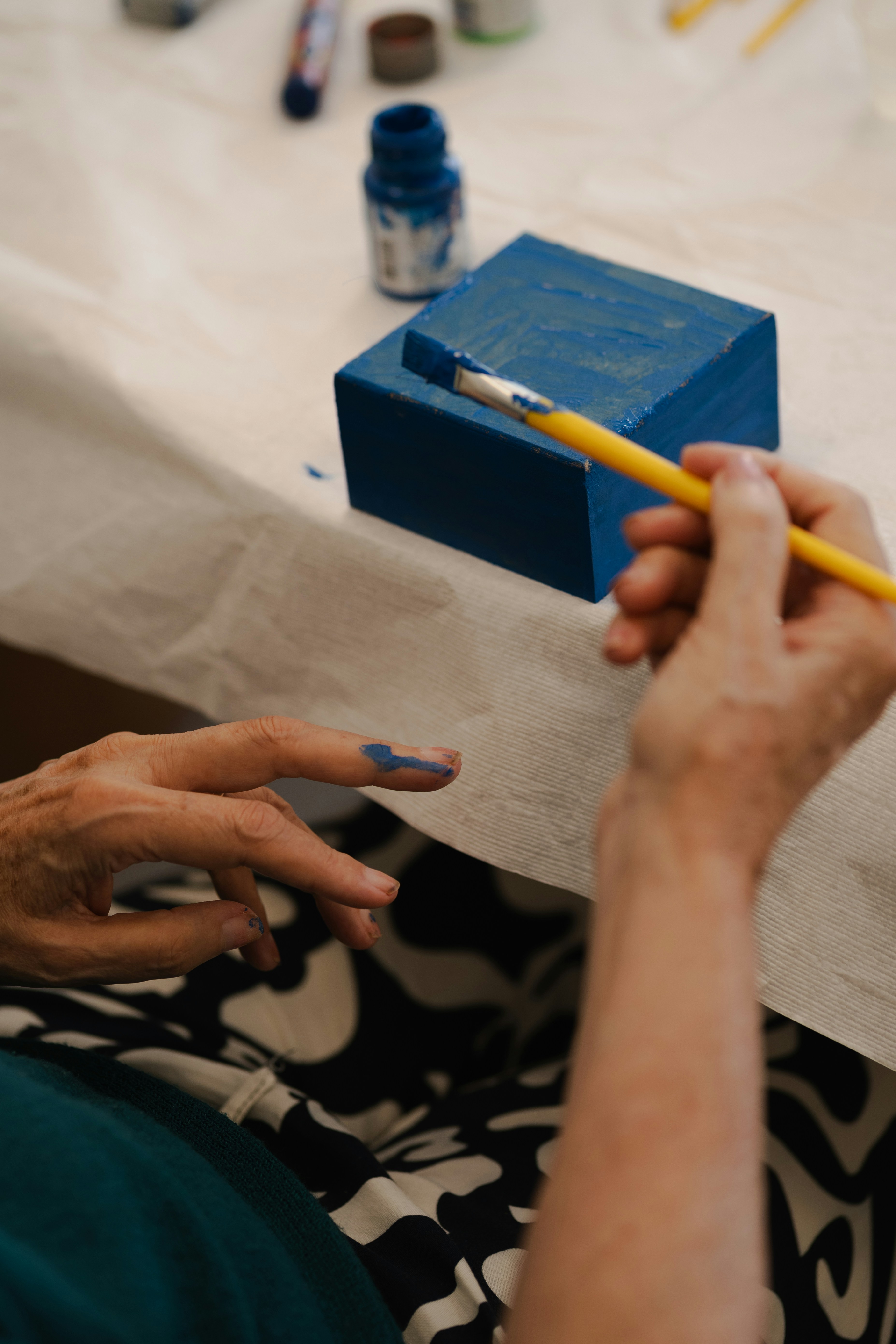 Eine Person, die einen Pinsel mit blauer Farbe am Finger in der Nähe eines blauen Blocks hält