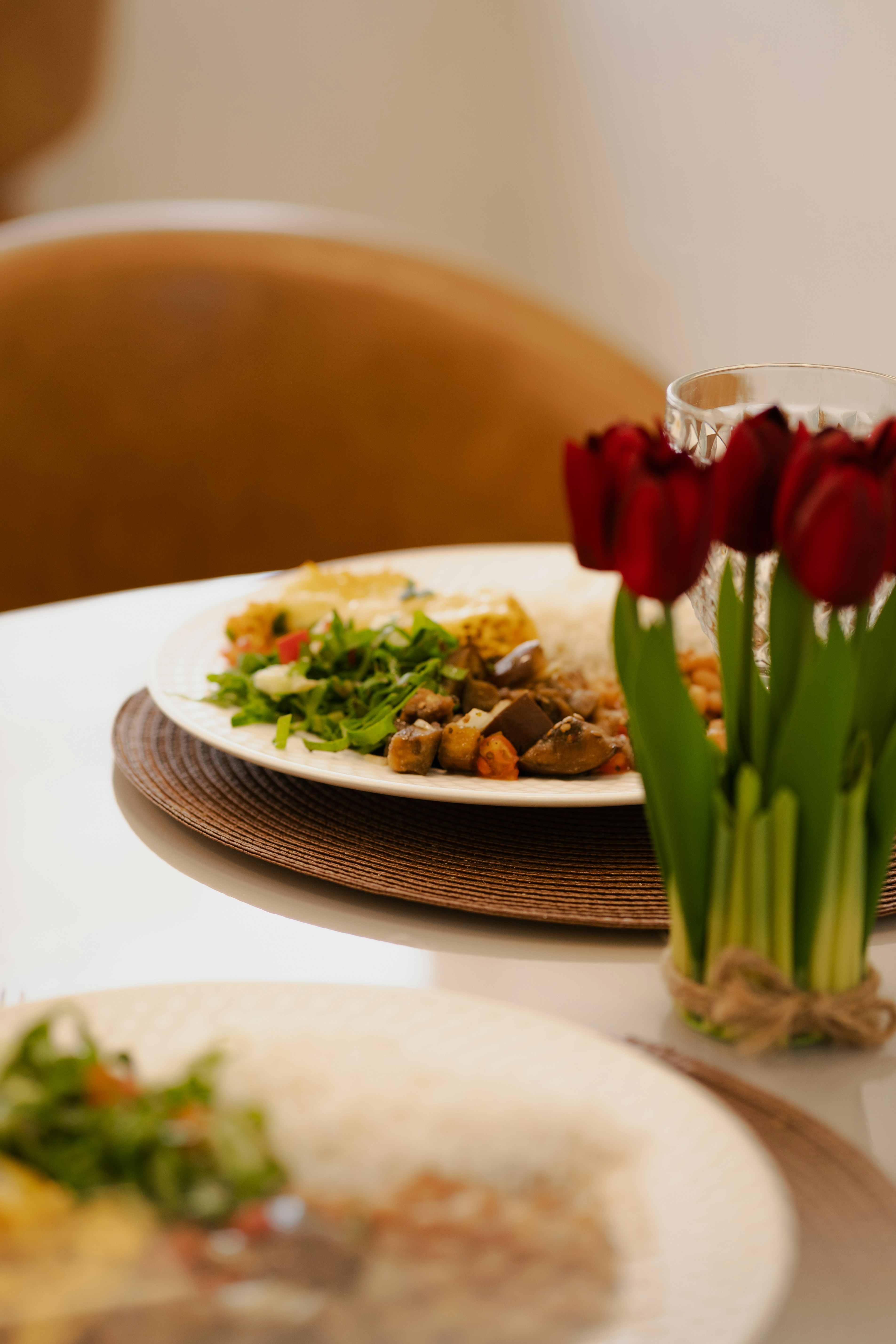 Teller mit Speisen mit Salat und Reis neben einer kleinen Vase mit roten Tulpen