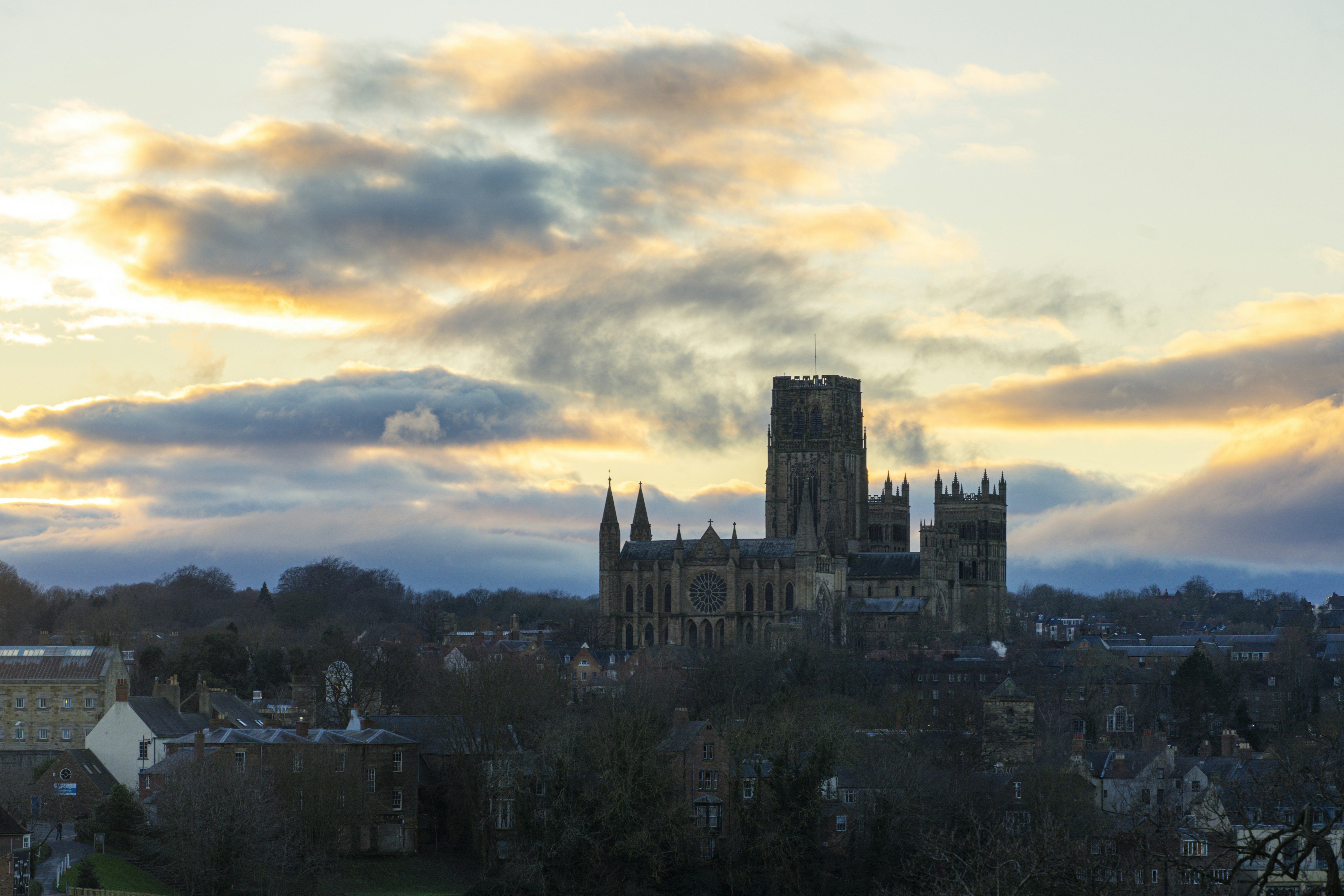 Durham Cathedral rising above a town under a sky with golden hour clouds