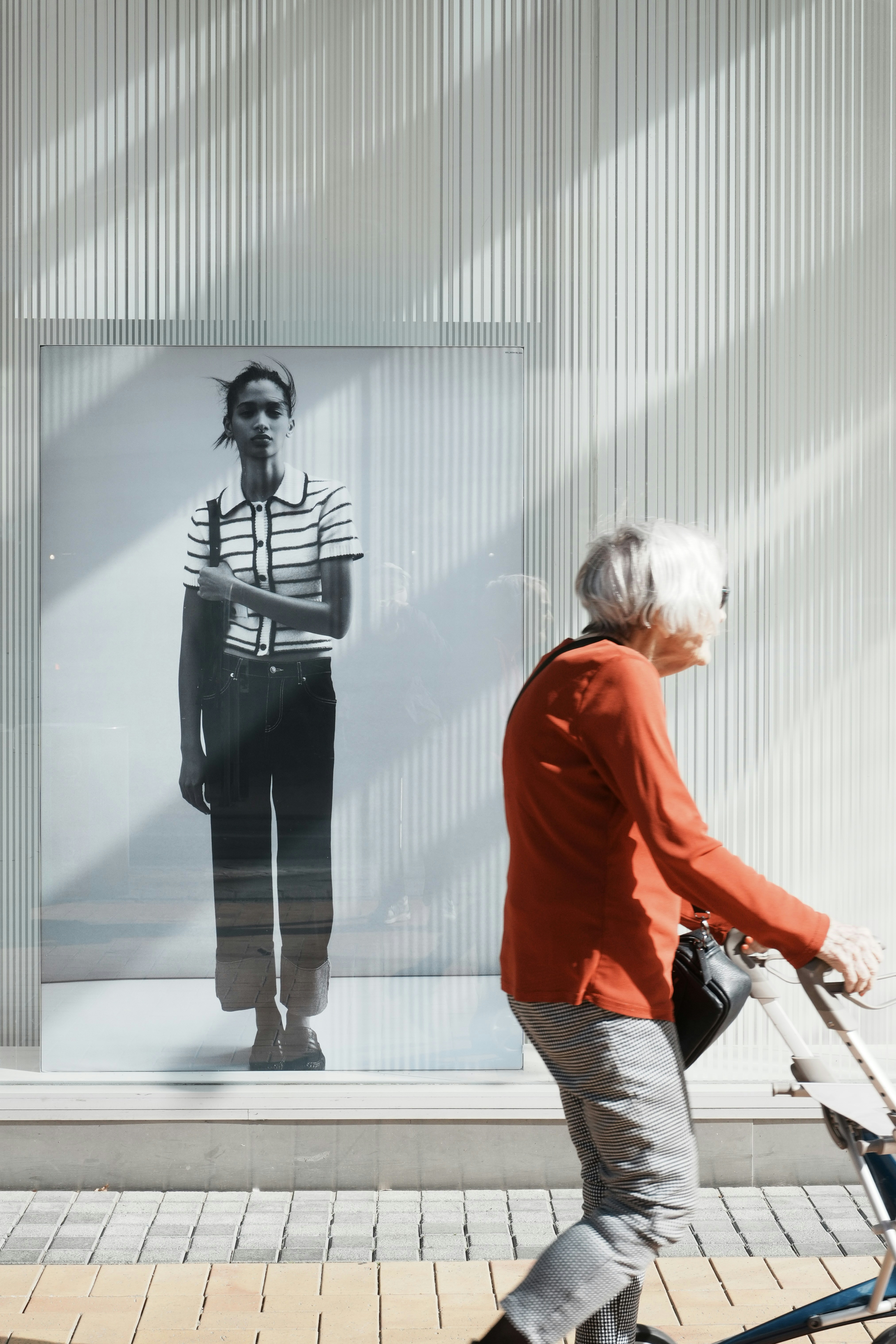 An older person with white hair walking past a large fashion advertisement poster