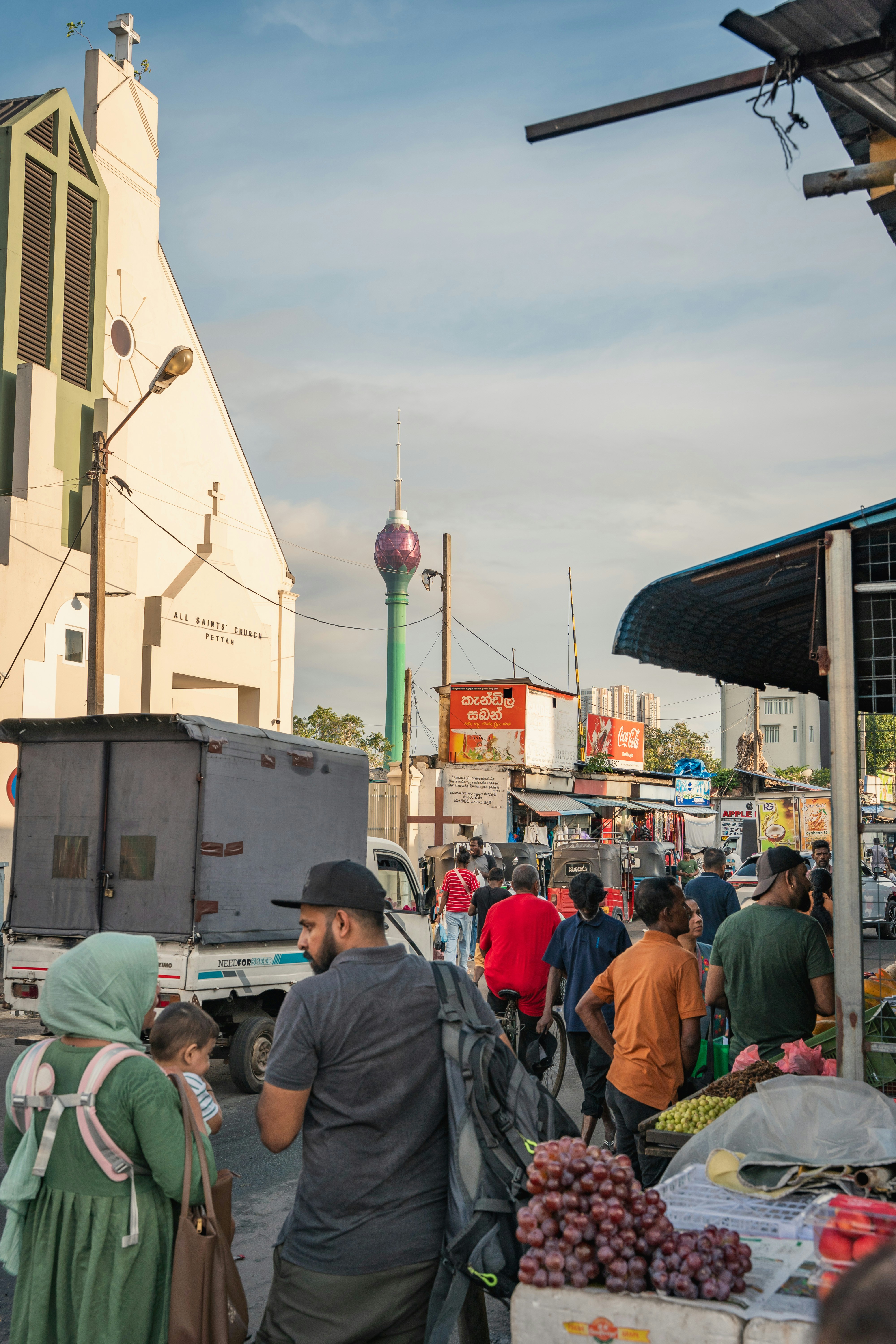 People walking on a busy street in Colombo with All Saints Church and Lotus Tower
