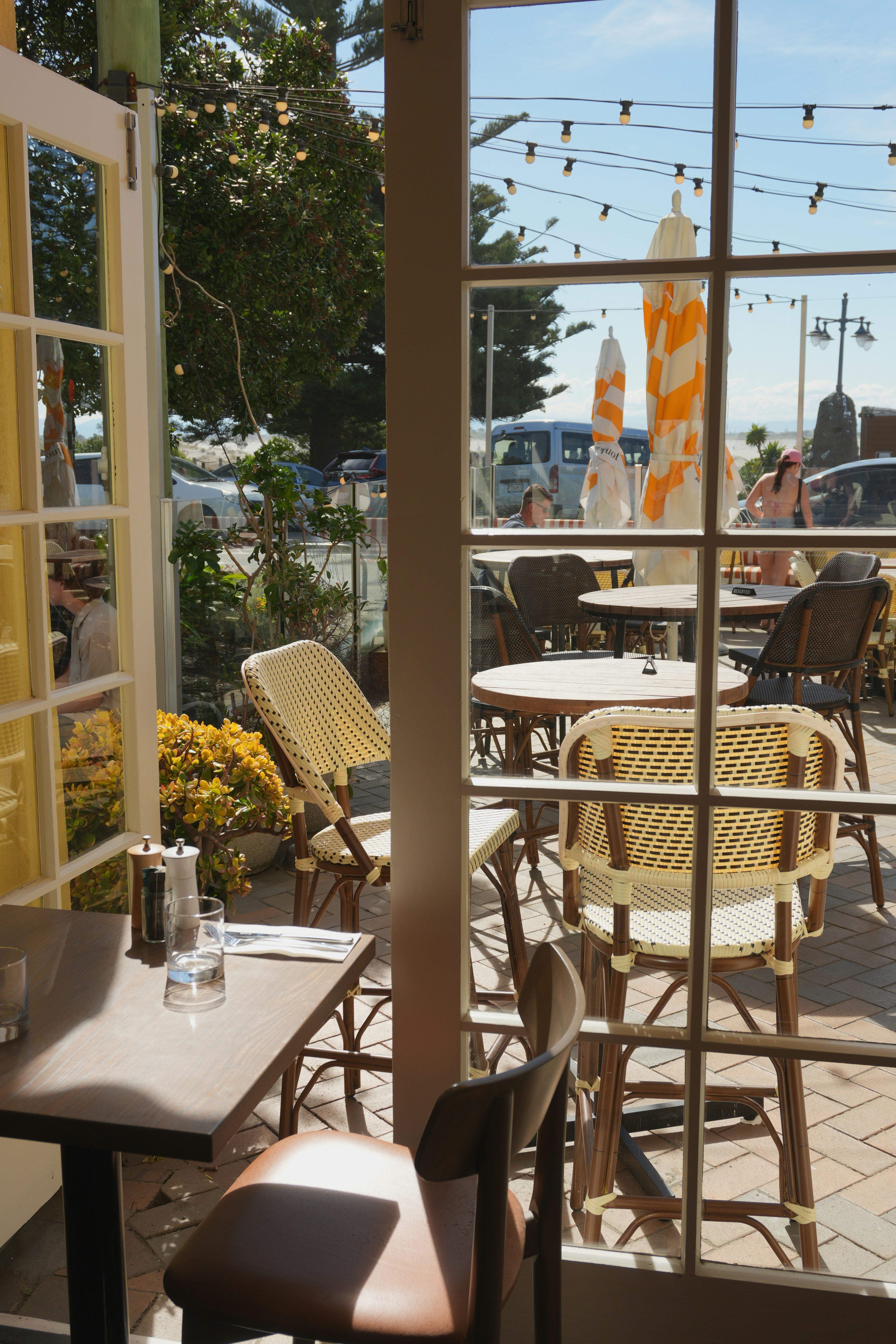 Woven chairs and wooden tables on a sunlit outdoor patio at a cafe