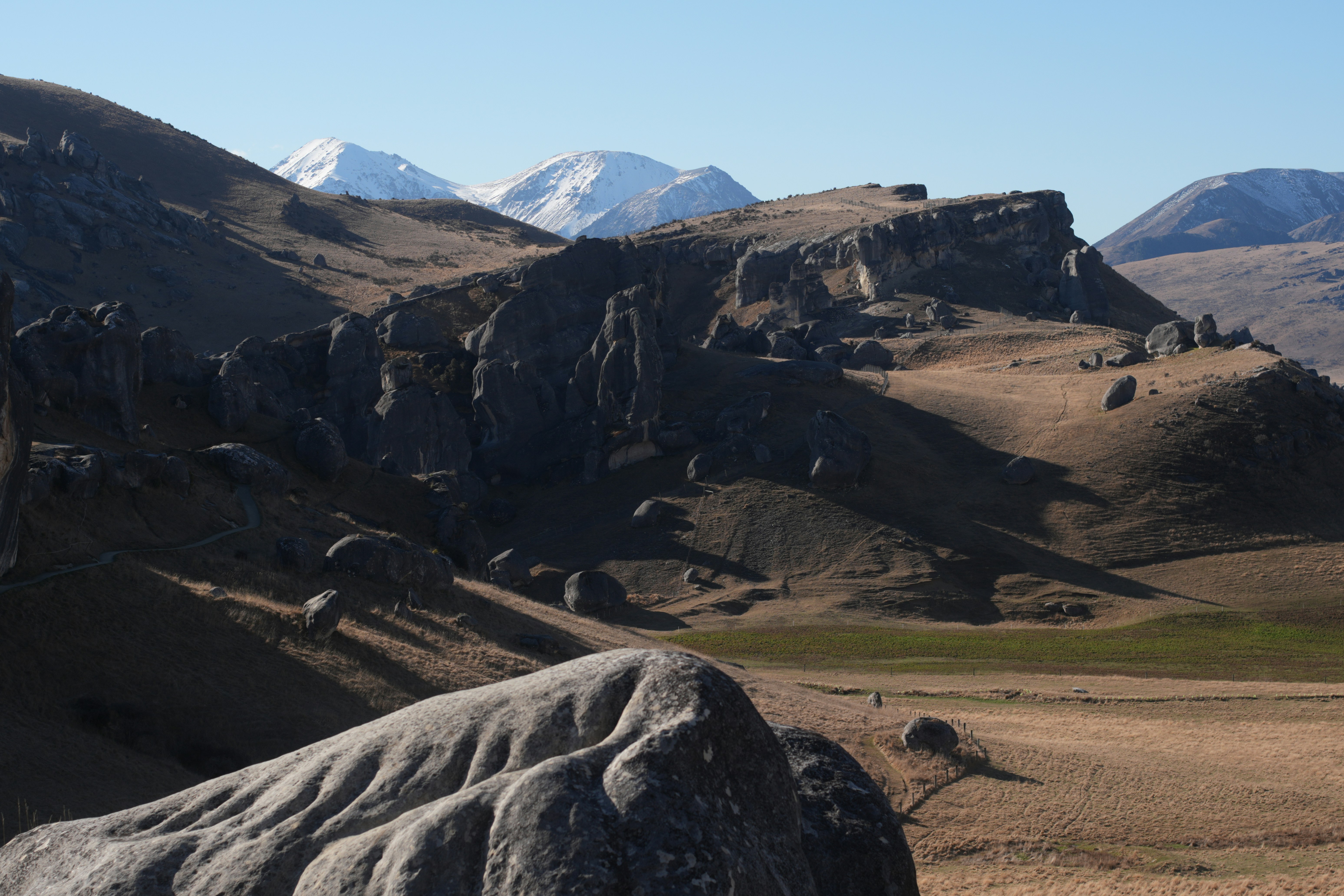 Large limestone boulders scattered across a dry grassy hillside with snow-capped mountains behind