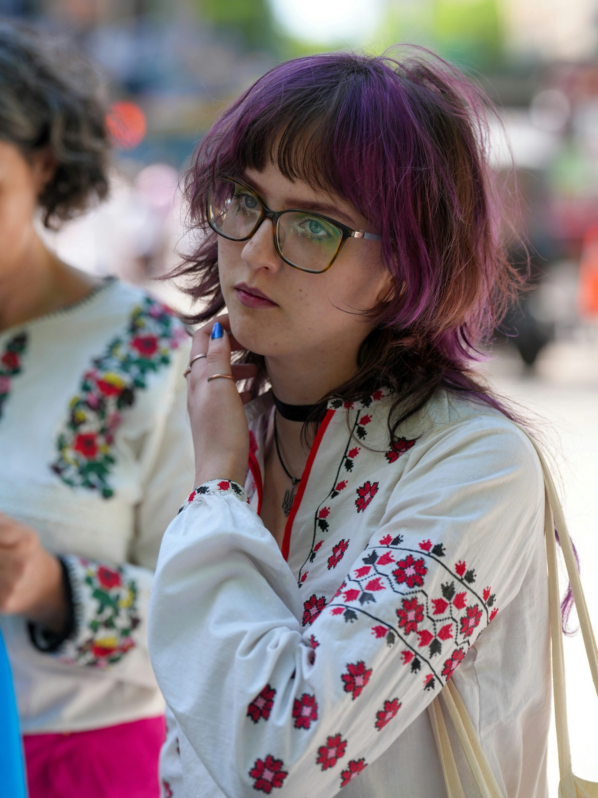 A person with purple hair and glasses wearing a white embroidered shirt
