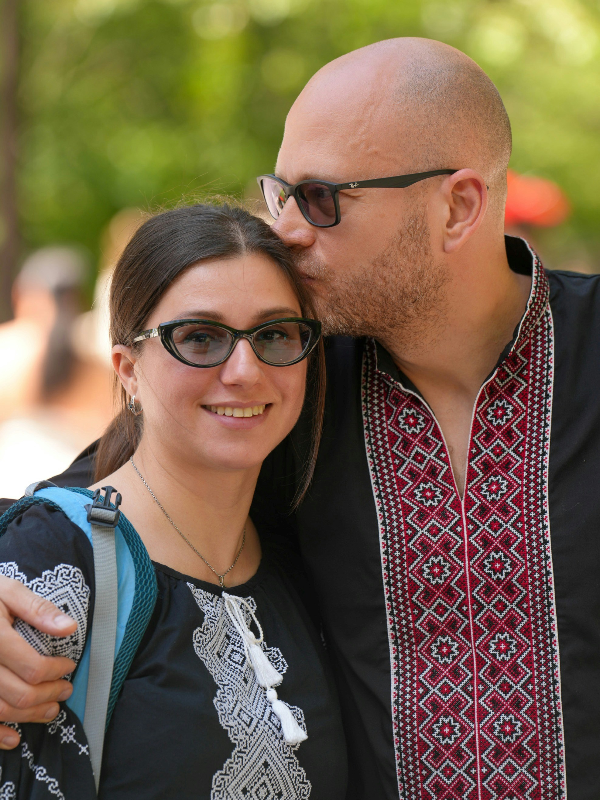 A man kissing a woman on the forehead, both wearing black embroidered shirts