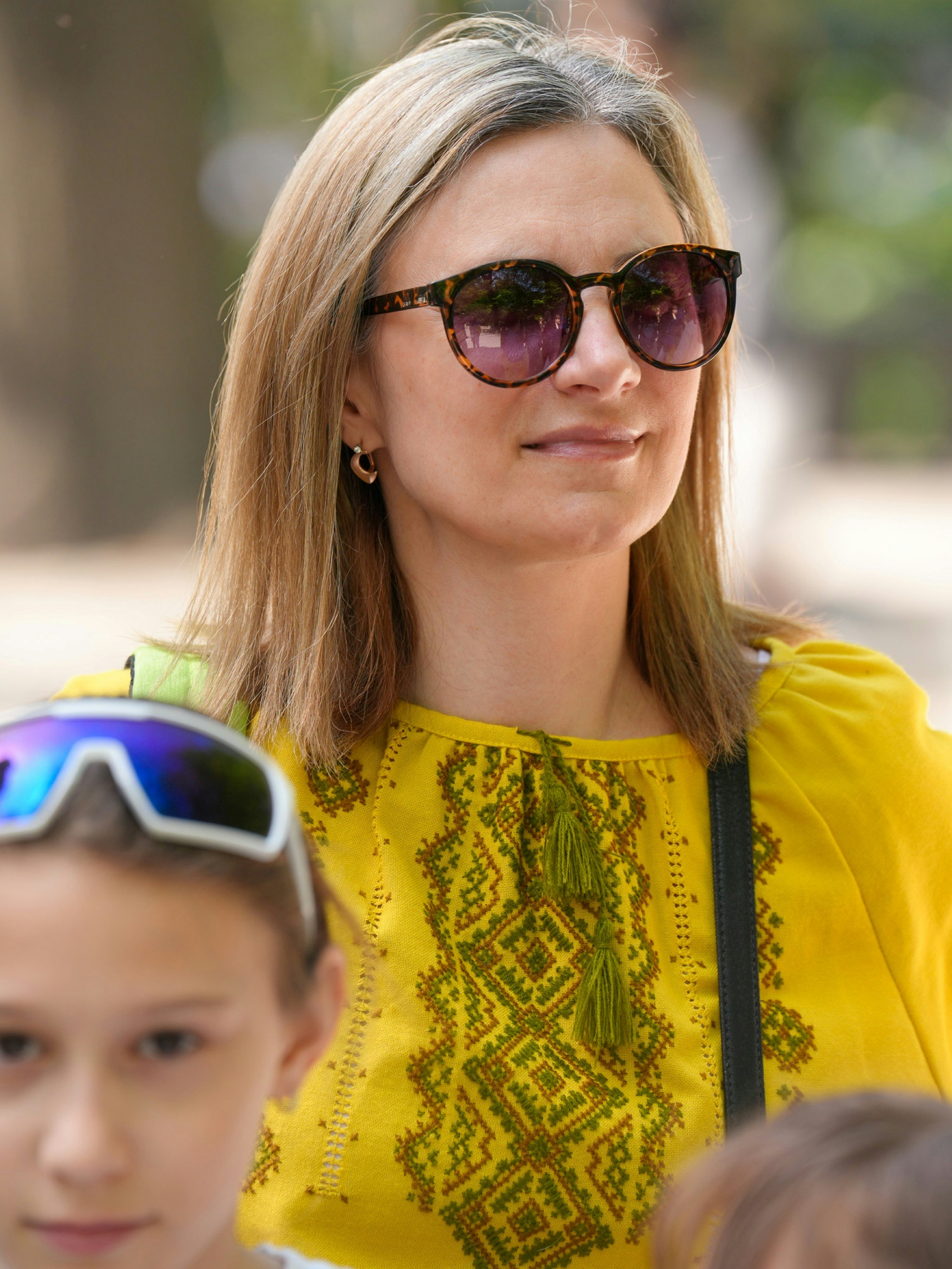 A woman wearing sunglasses and a yellow embroidered blouse with a child nearby