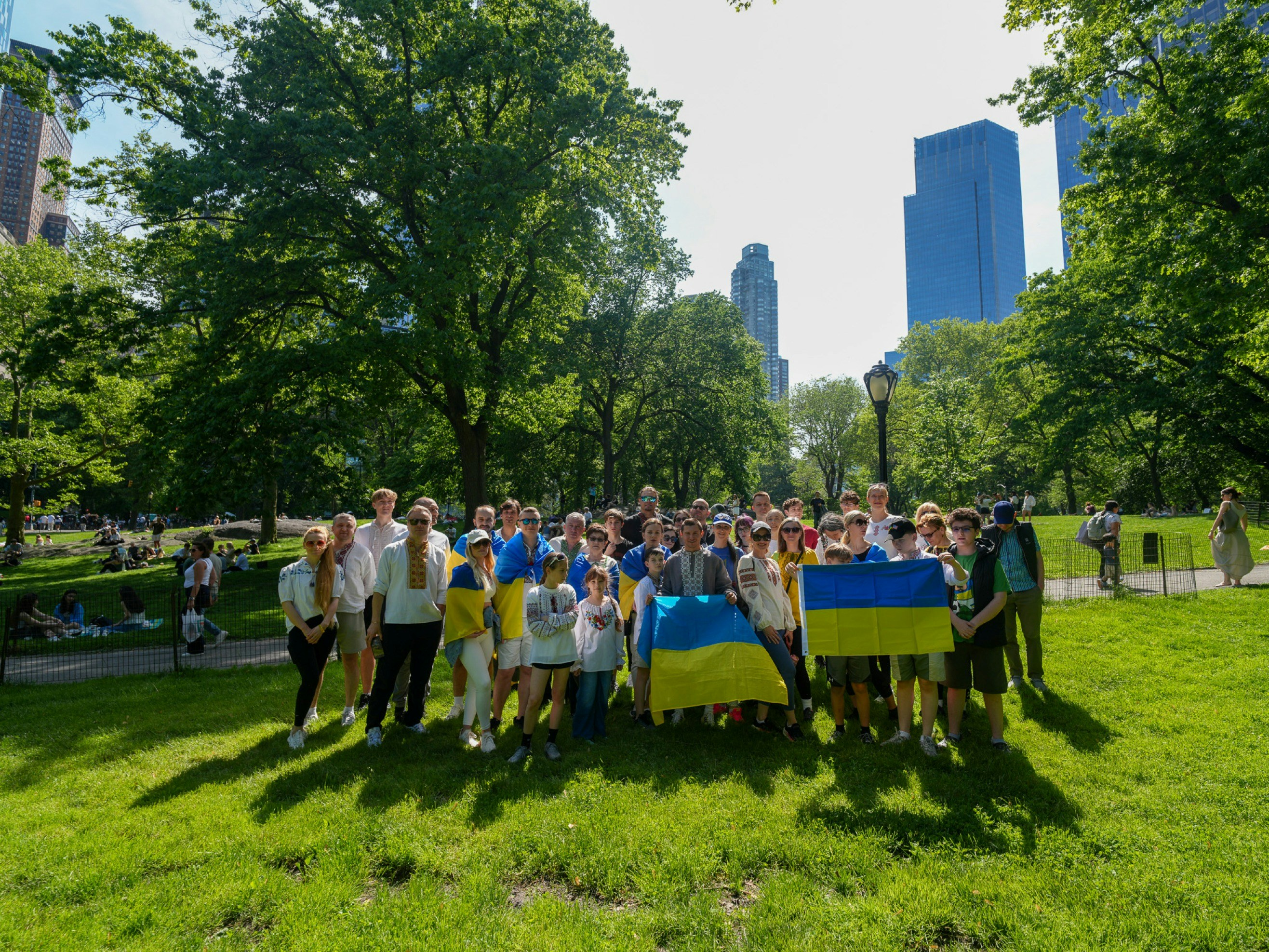 A group of people holding Ukrainian flags in a sunlit park in New York