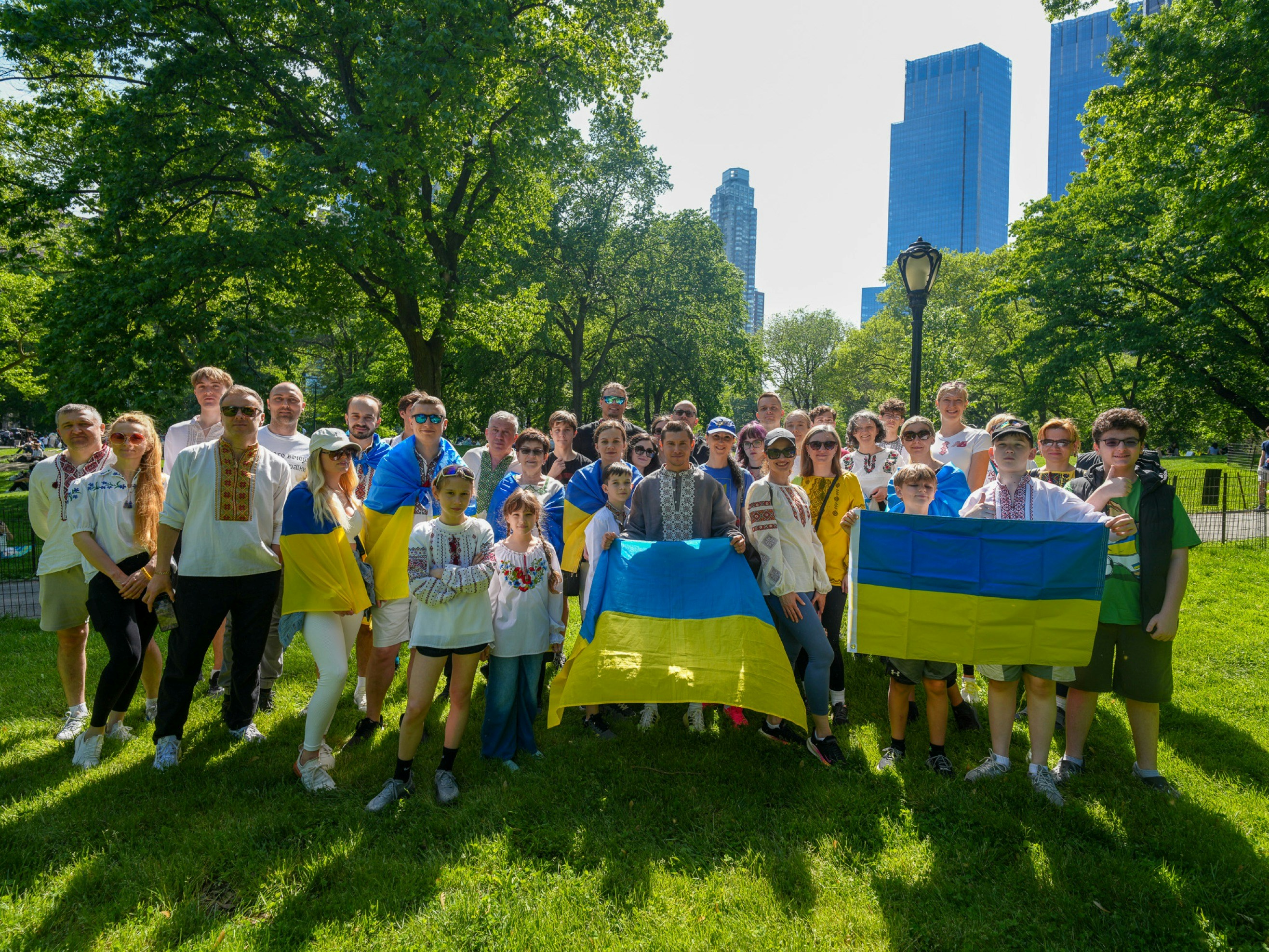 A group of people in embroidered shirts holding Ukrainian flags in a sunny park