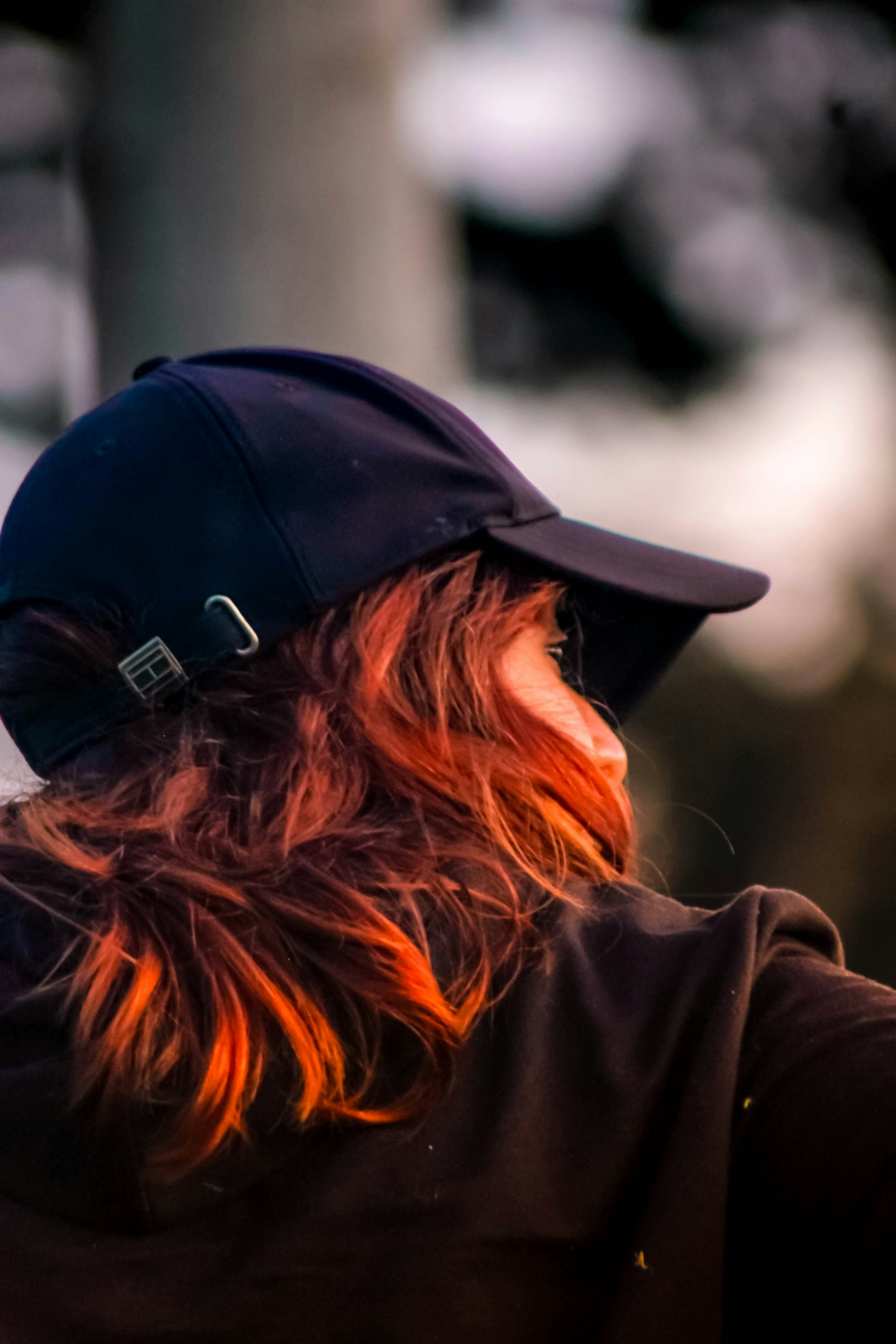 A person with red-tinted hair wearing a dark baseball cap in soft light