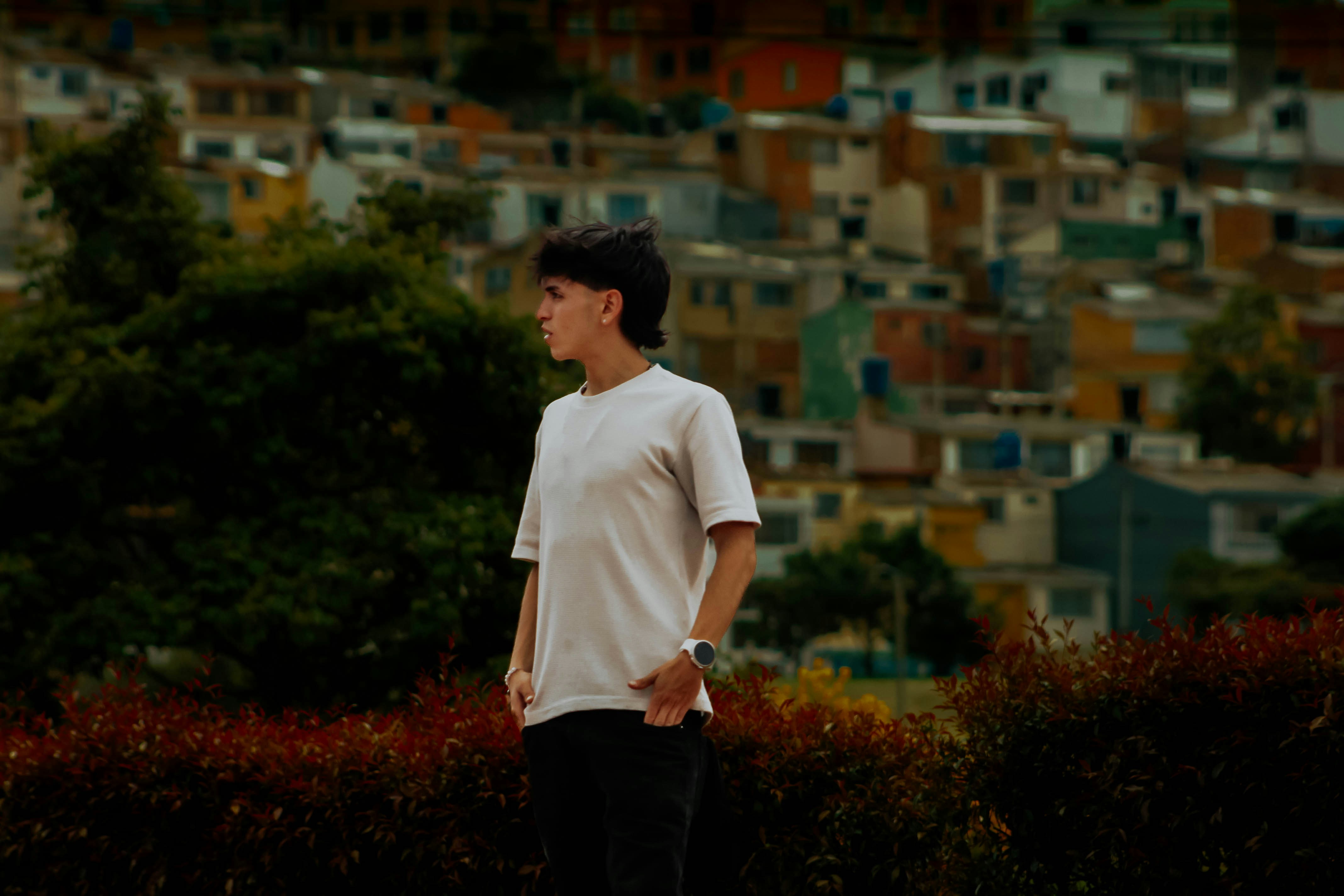 A young man in a white t-shirt standing before a hillside of houses