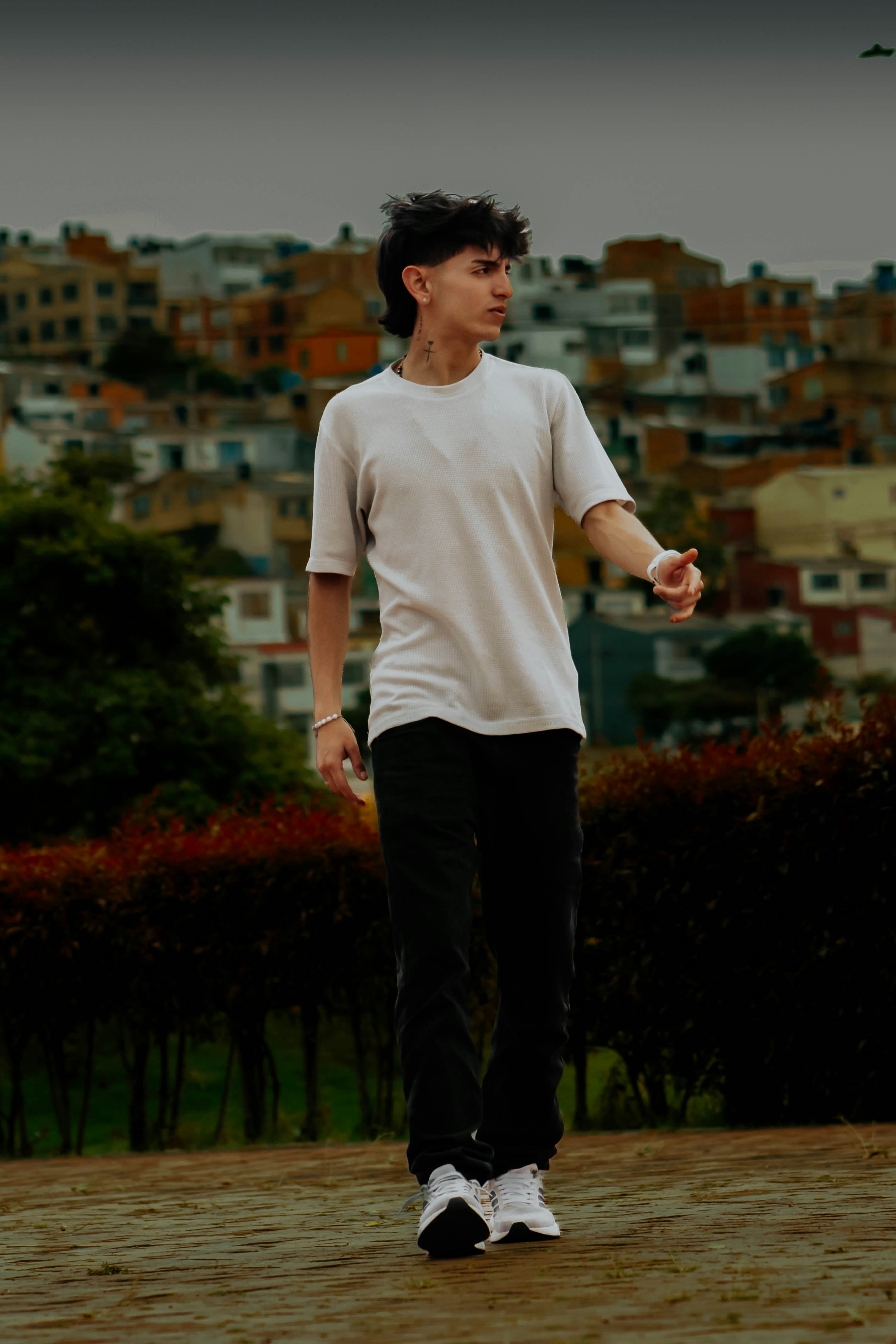 A young man in a white t-shirt and black pants walking outdoors