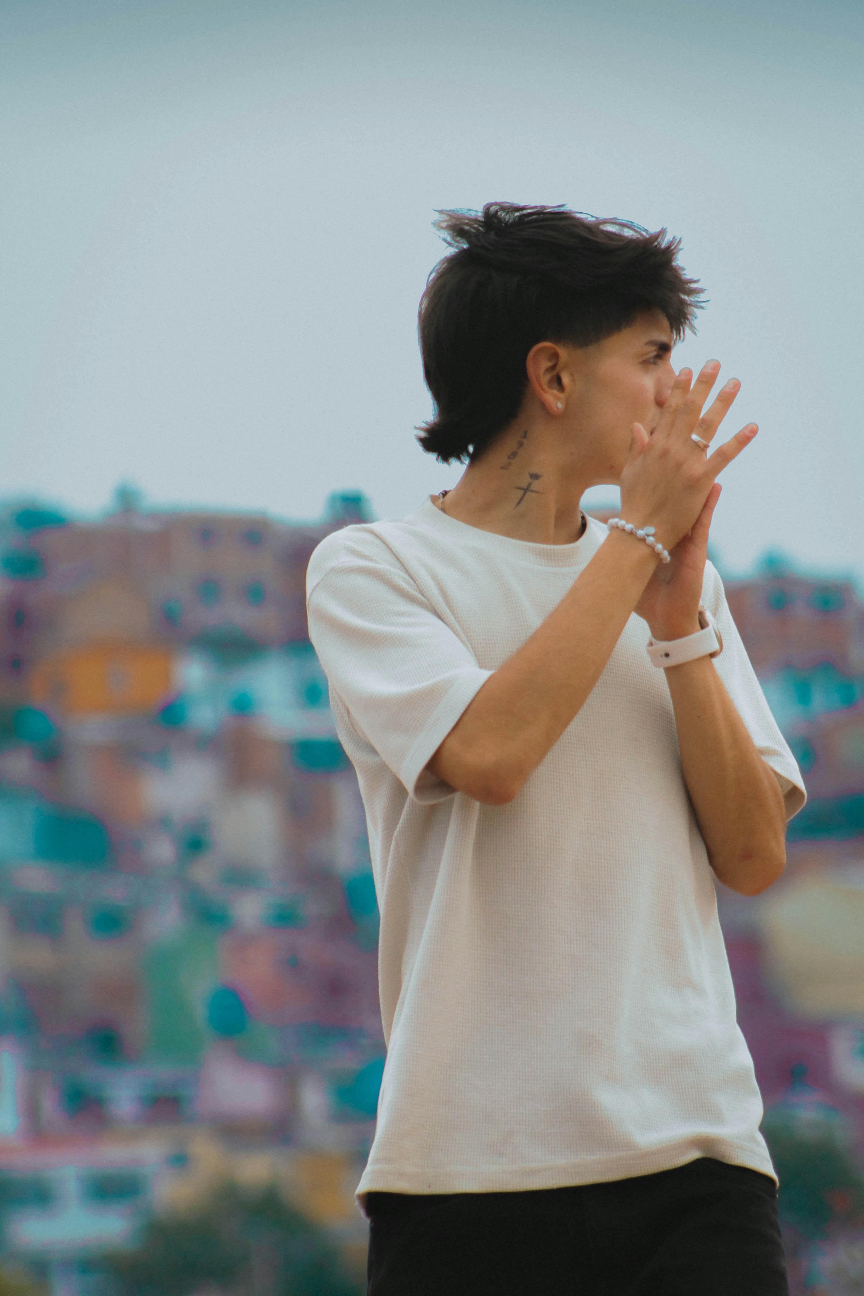 A person with a neck tattoo wearing a white t-shirt against a blurred cityscape