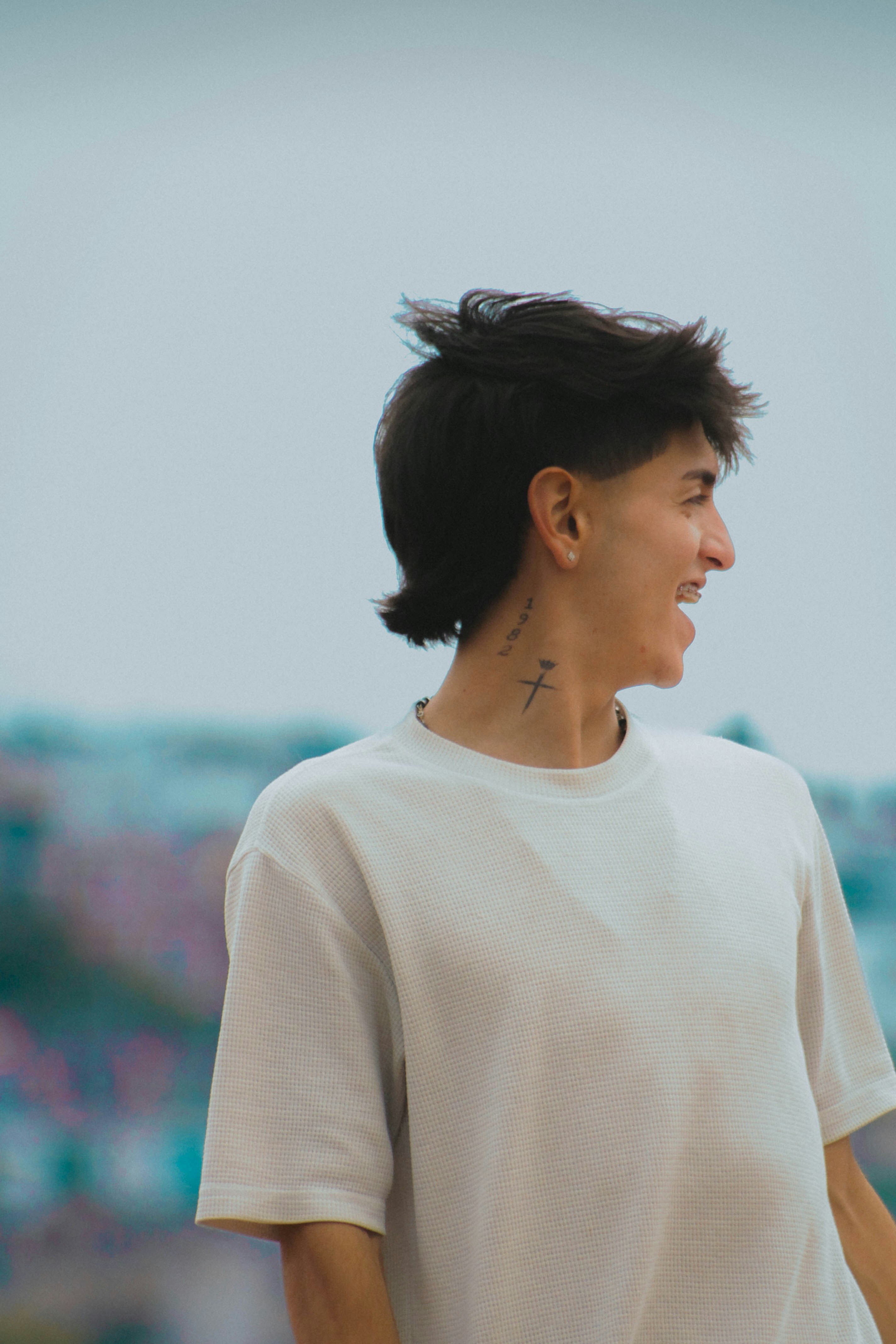 A person with a dark mullet and neck tattoos in a white t-shirt