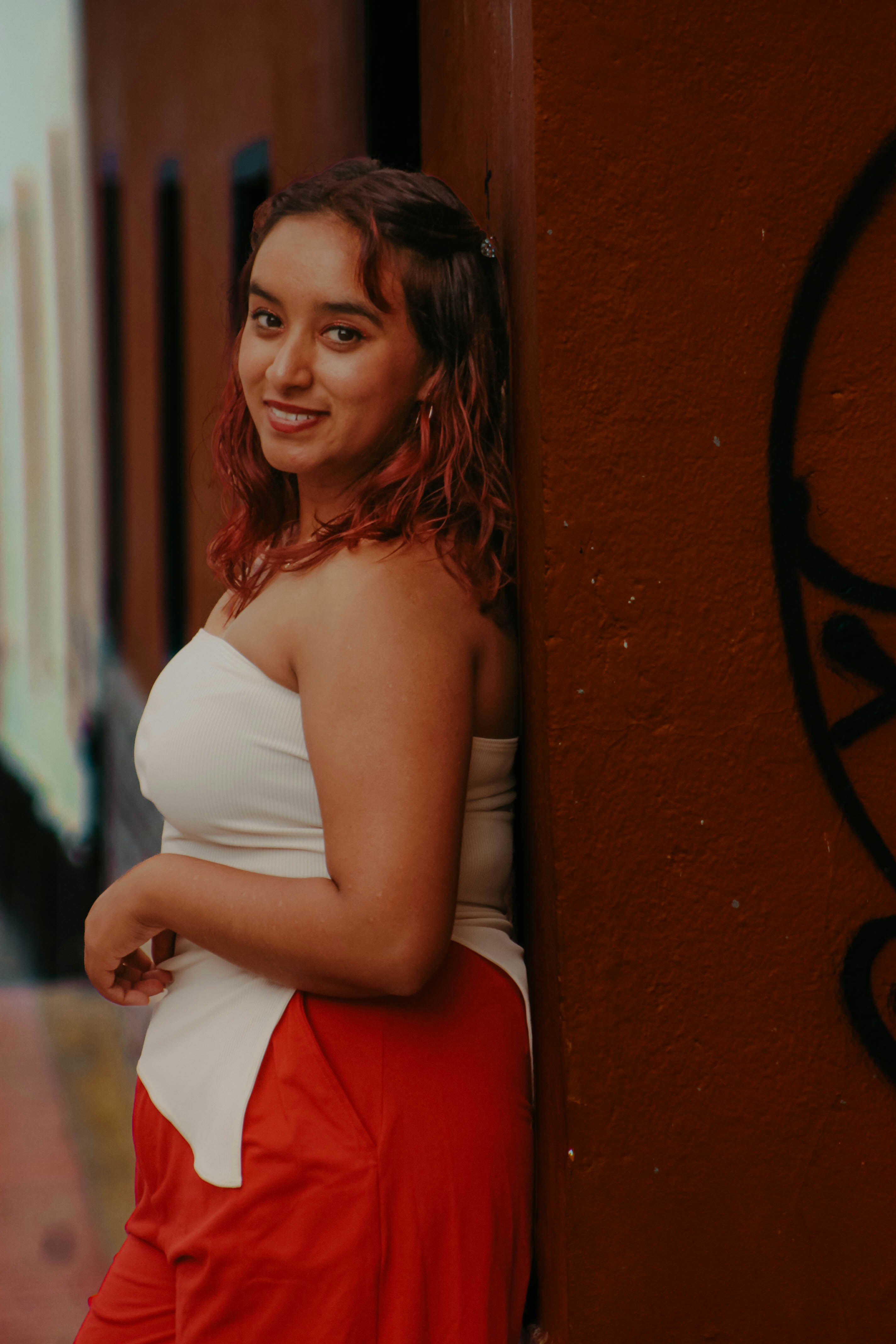 A woman with reddish hair in a white tube top and red pants