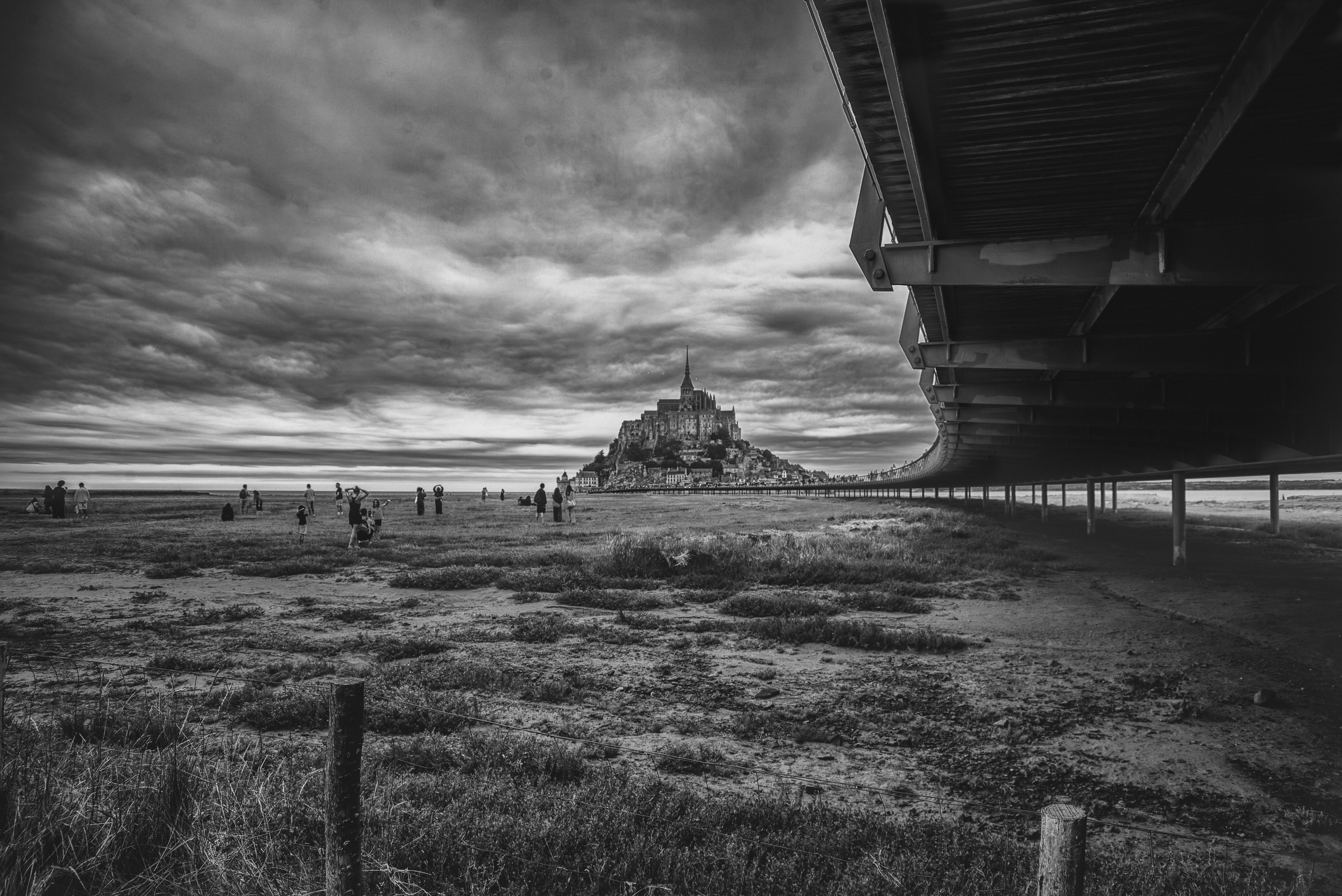 Mont Saint-Michel in the distance under a cloudy sky with people on the flats