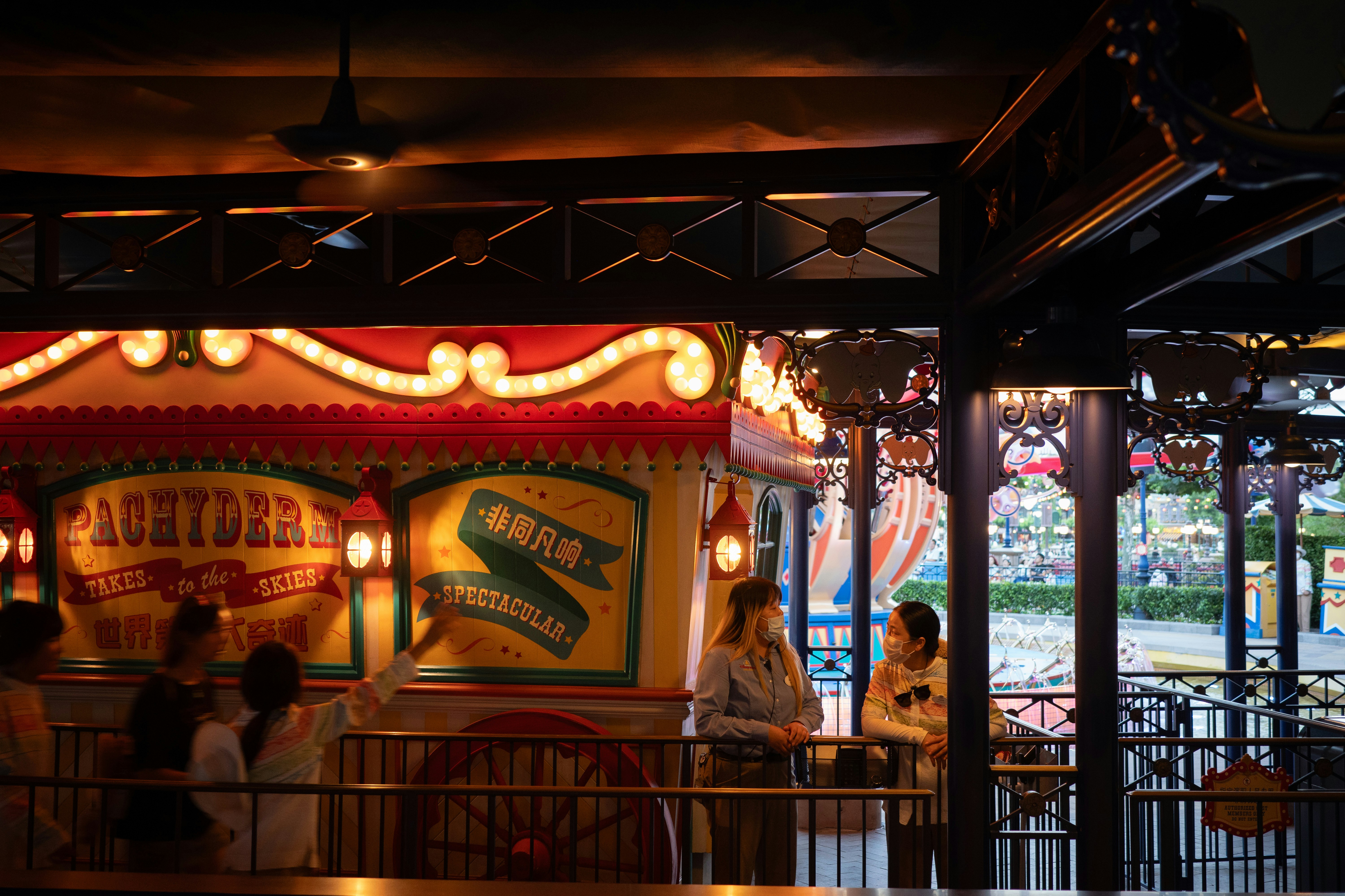 Two people in face masks talking near a colorful carnival ride at night