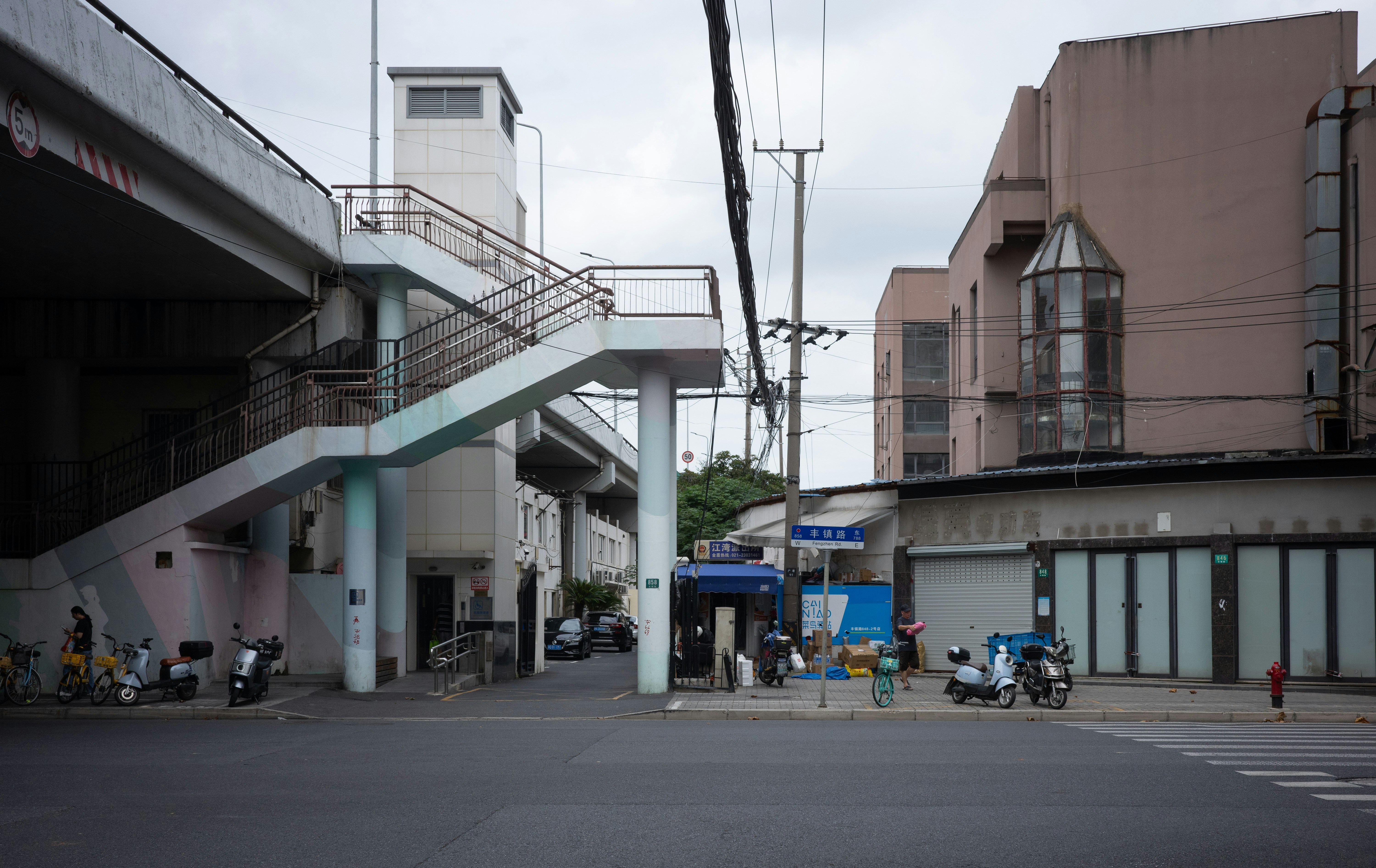 A street intersection with a pedestrian overpass, parked scooters, and urban buildings