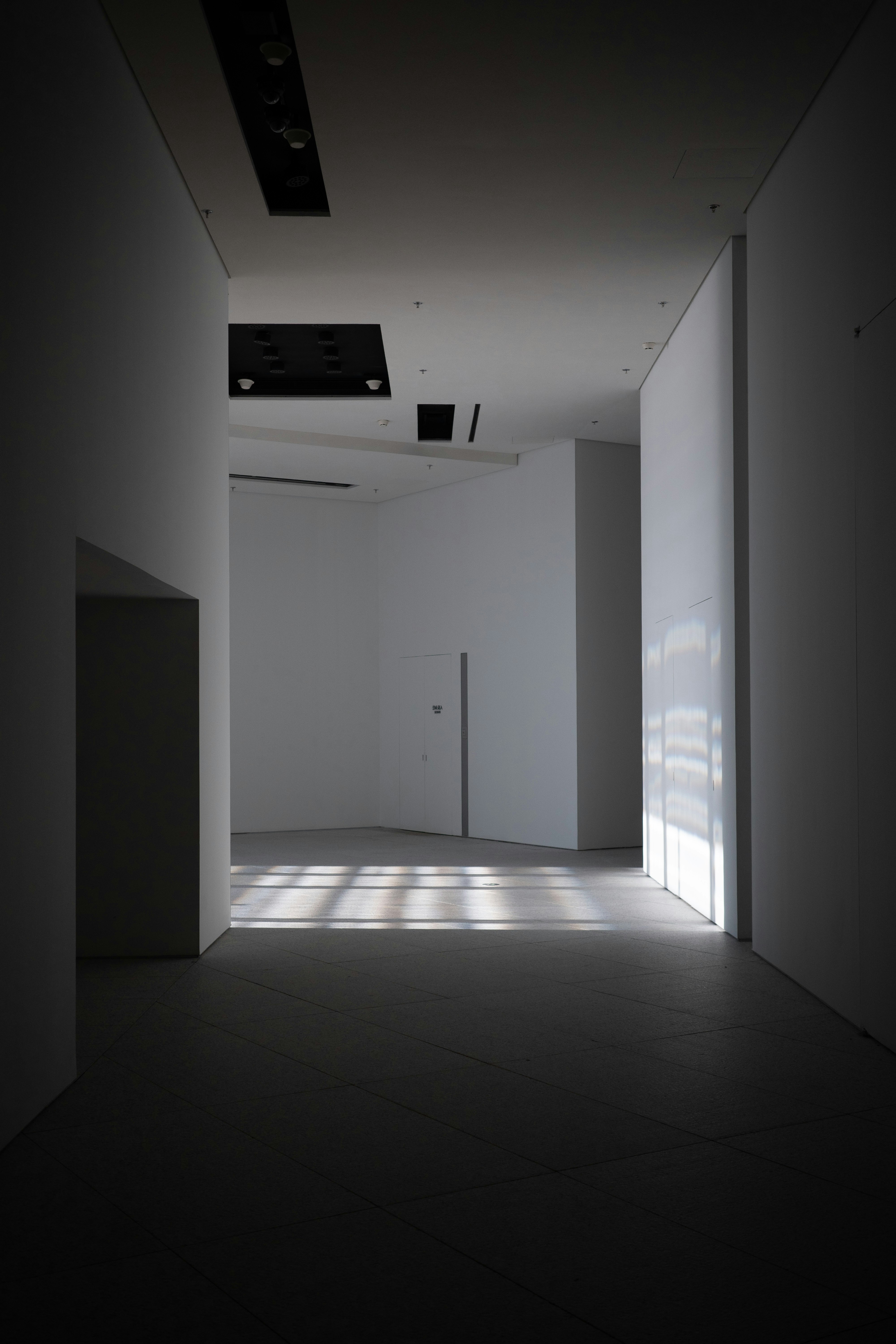 A minimalist white hallway with geometric light patterns cast across the floor