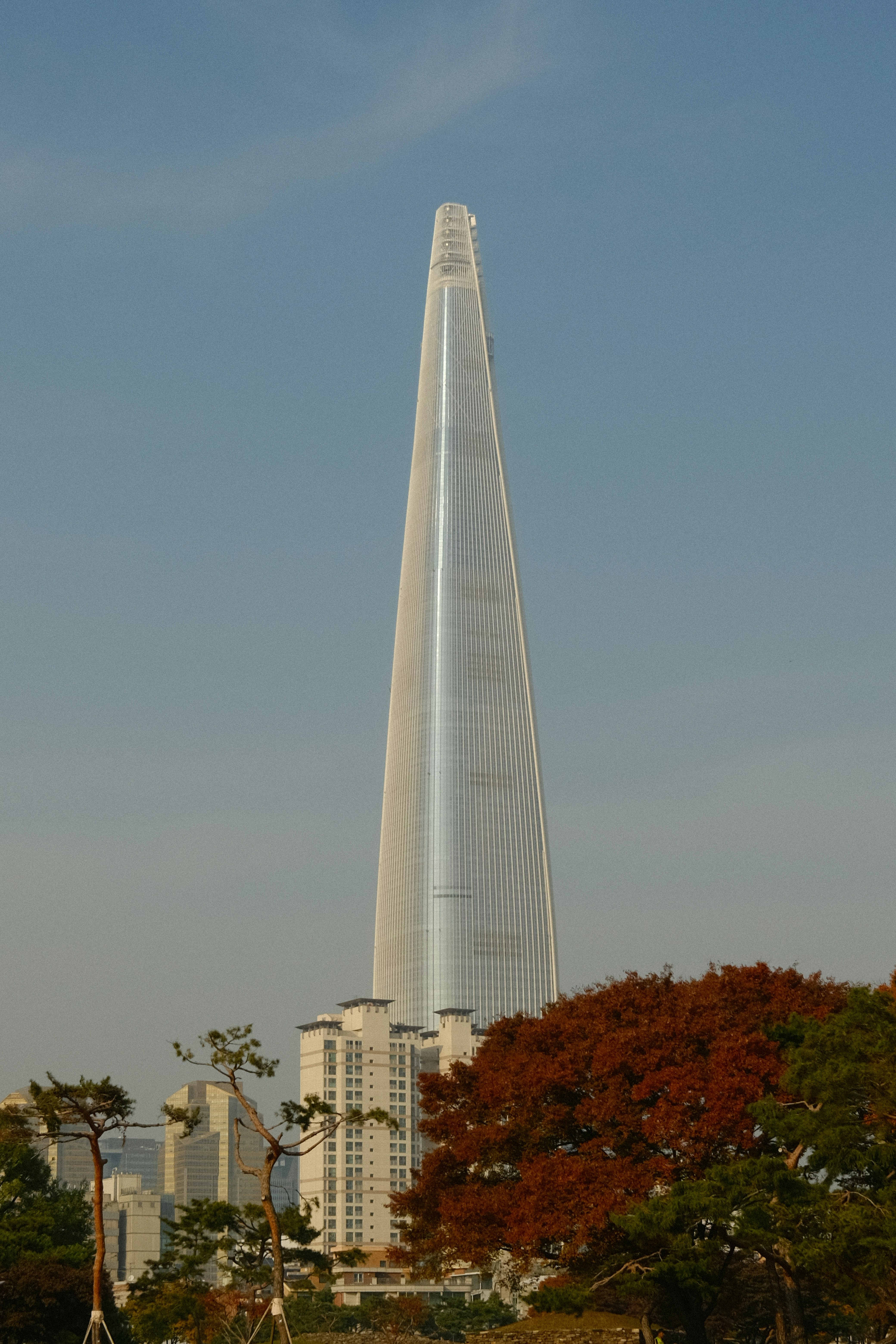 The Lotte World Tower rising above autumn trees and city buildings in Seoul