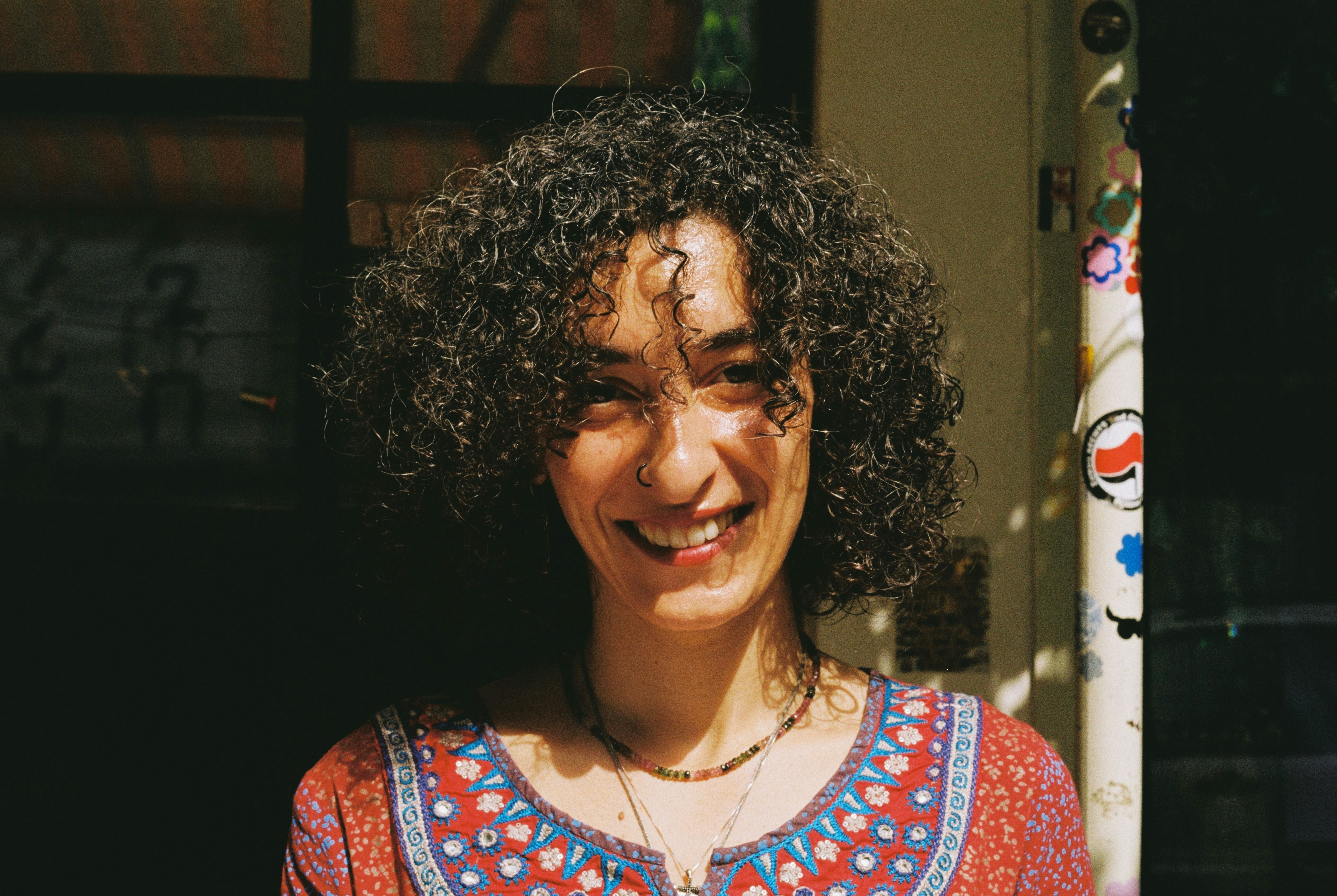 A smiling woman with curly dark hair and a nose ring in a patterned top