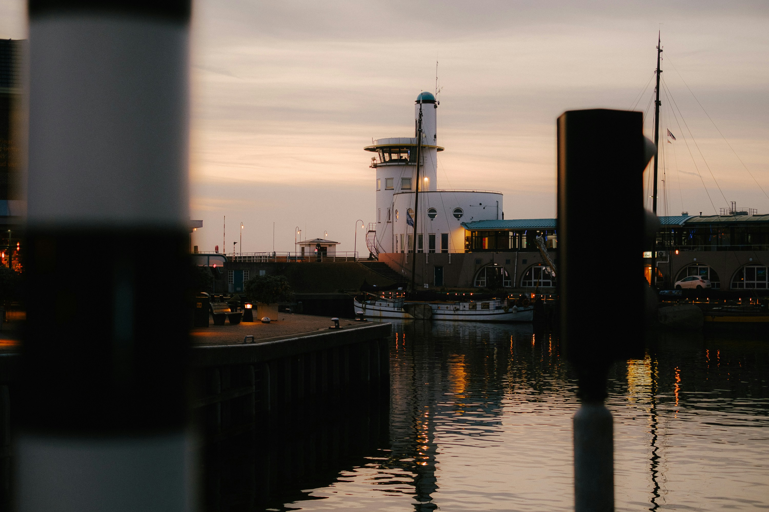 A white lighthouse tower overlooking a harbor at low sun with calm water