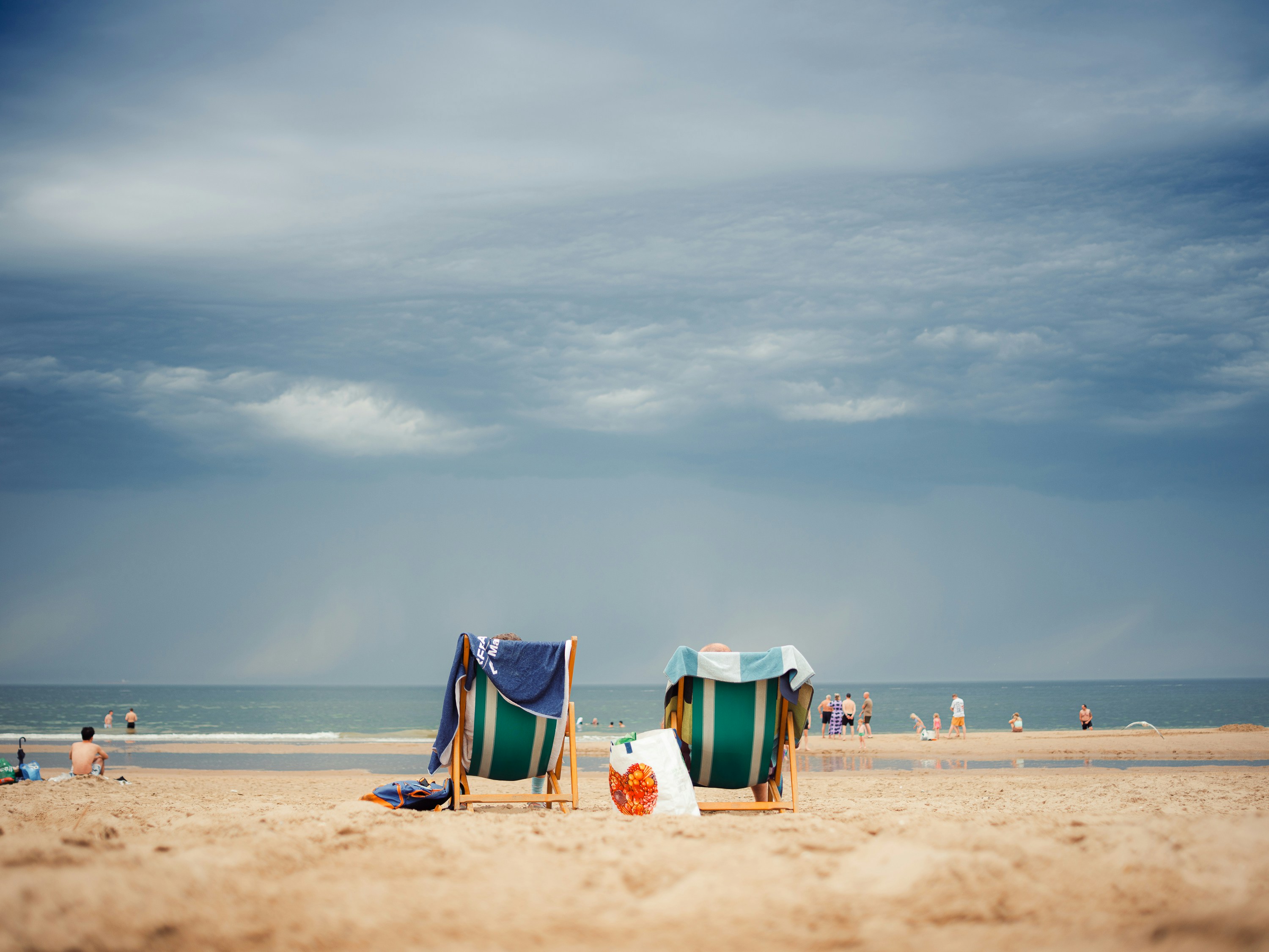 Two striped deckchairs on a sandy beach under a dark, cloudy sky