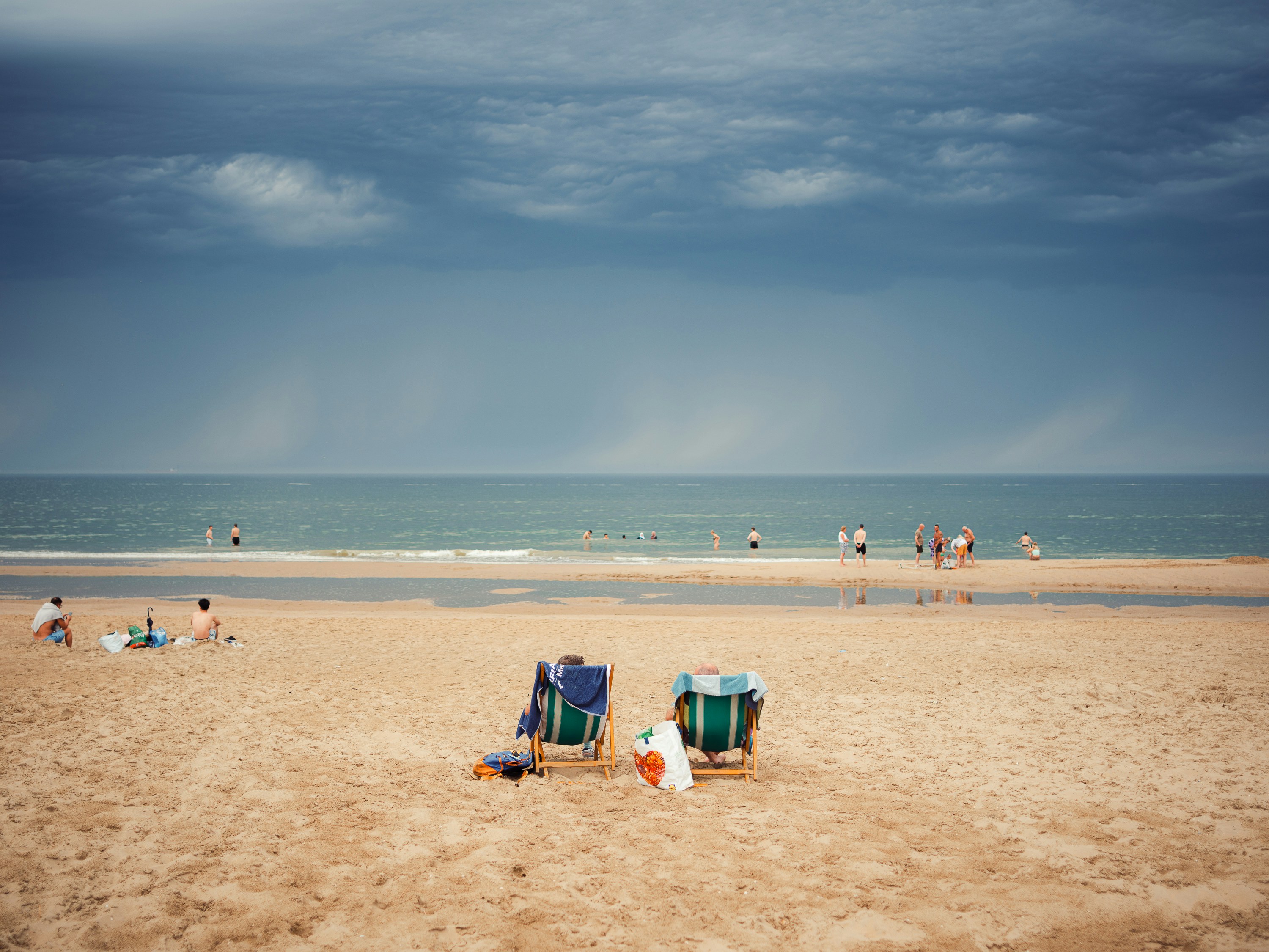 People on a sandy beach under a dark, stormy sky with rain clouds