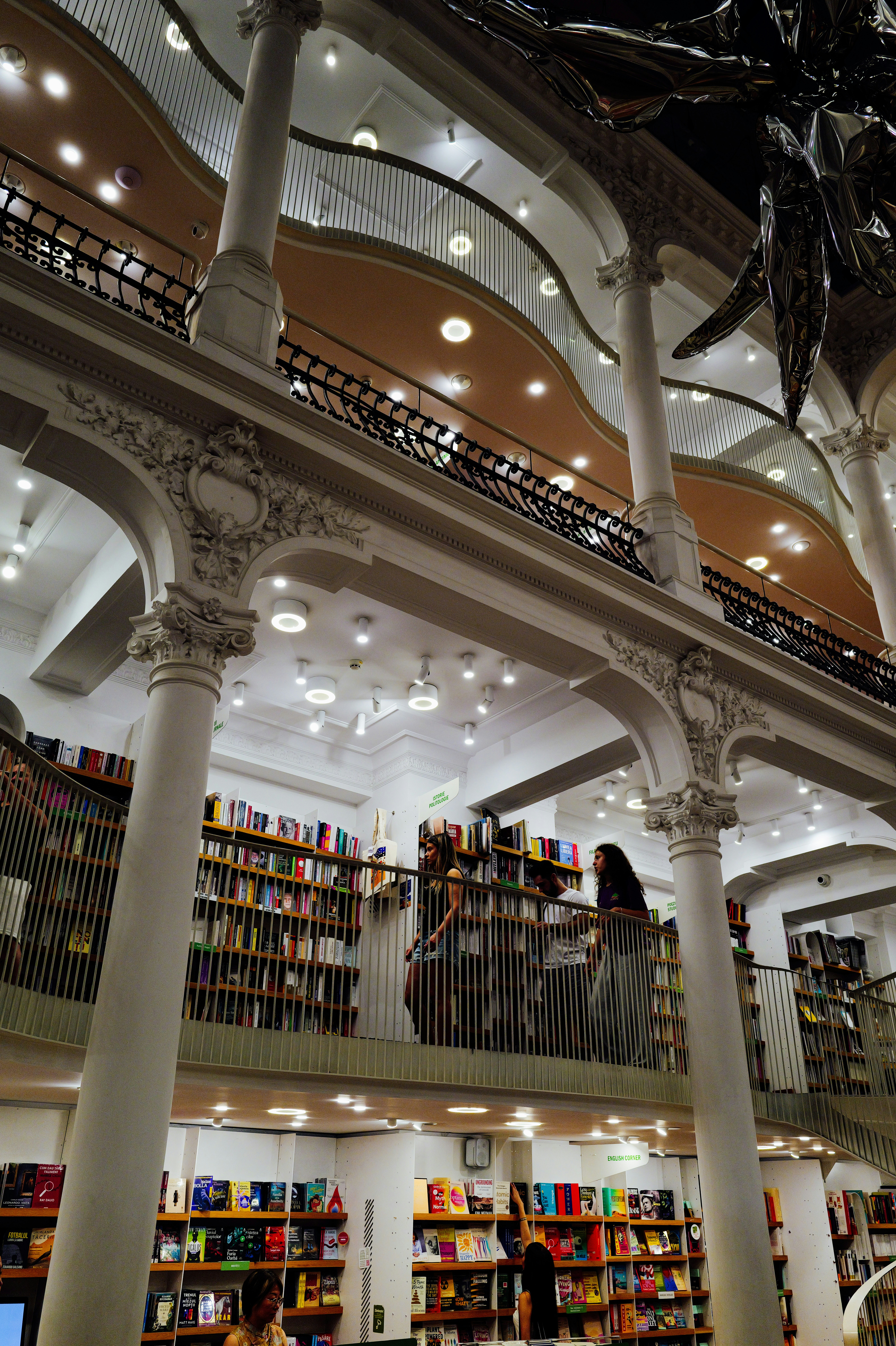 People browsing bookshelves on the mezzanine level of a grand multi-story bookstore