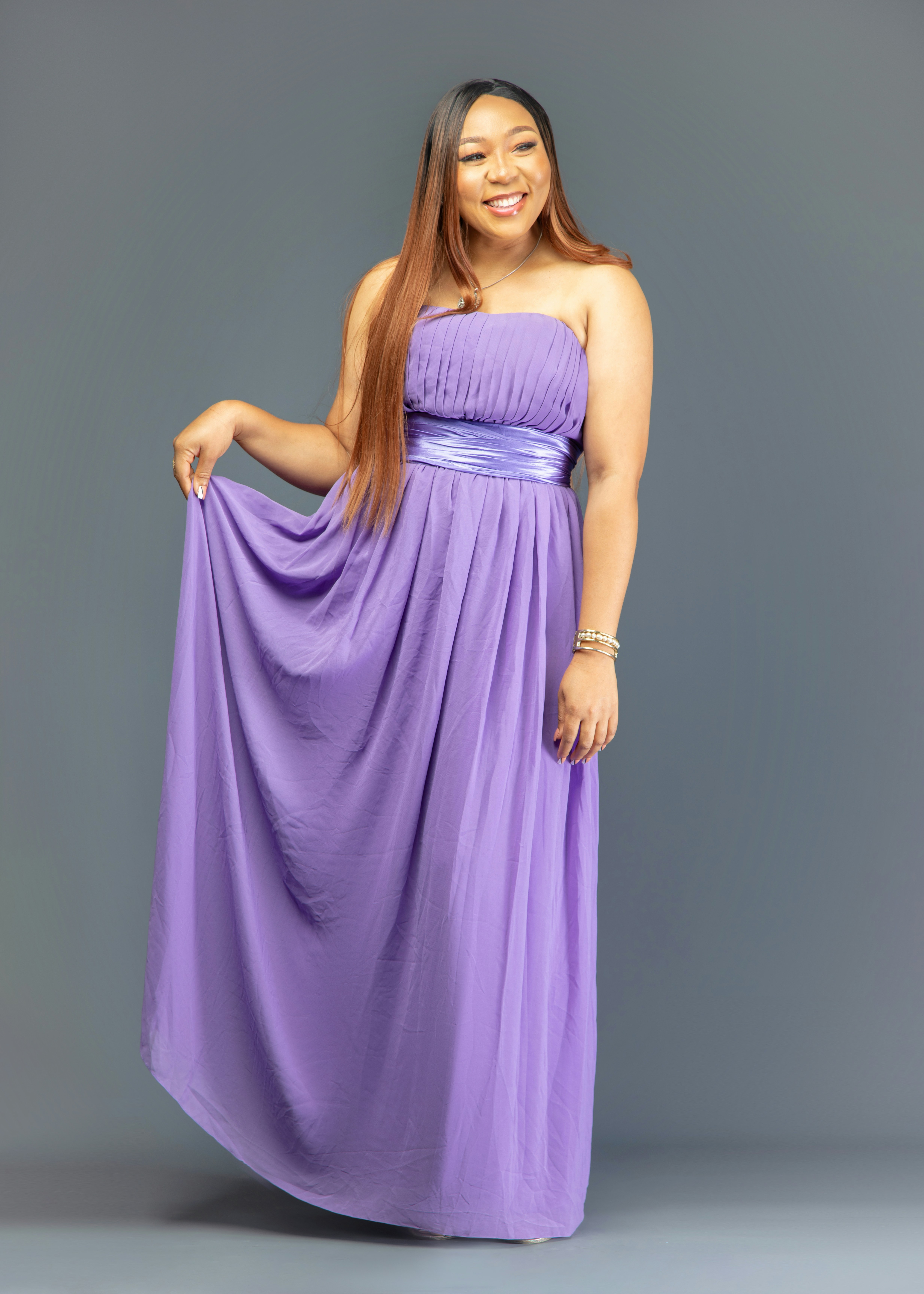 A woman in a strapless purple gown holding the skirt against a grey background