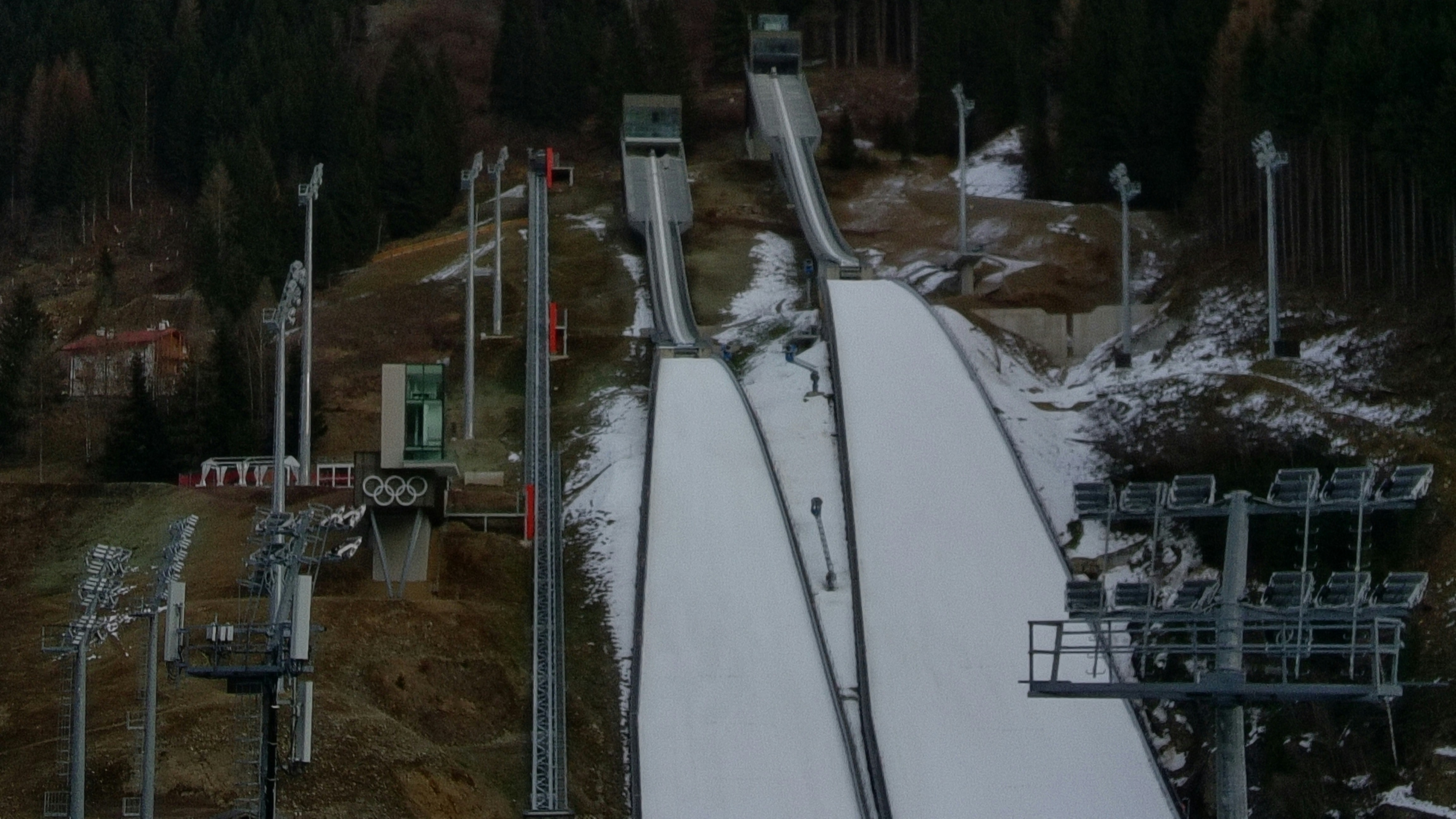 Two ski jumping ramps on a snowy hillside with tall stadium floodlights
